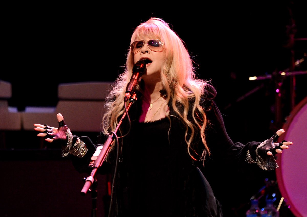 Stevie Nicks sings into a microphone wearing sunglasses.