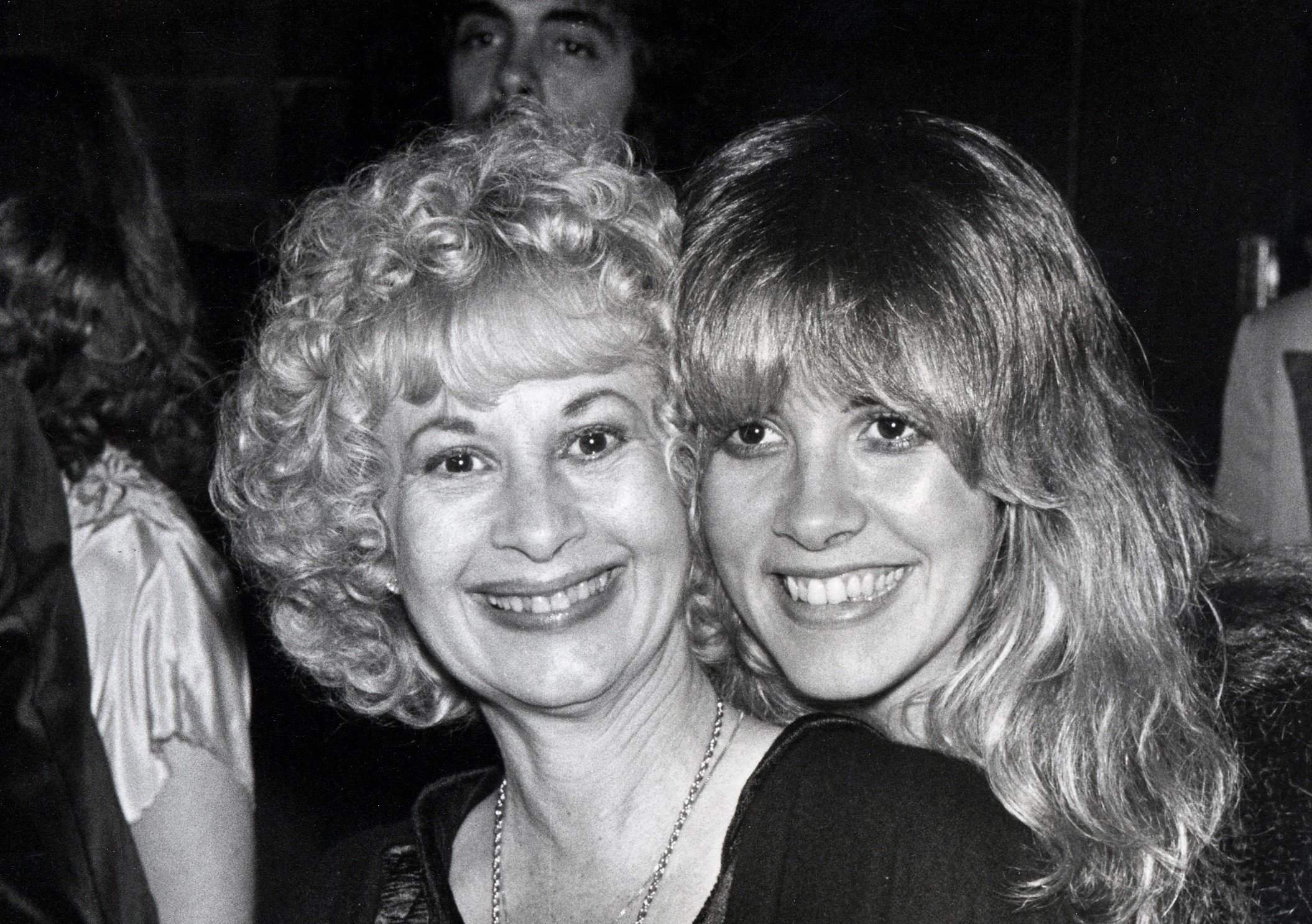 A black and white photo of Stevie Nicks and Barbara Nicks posing cheek to cheek. They both wear black.