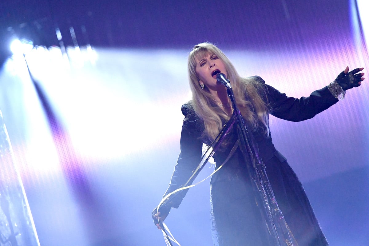Stevie Nicks sings into a microphone on stage.