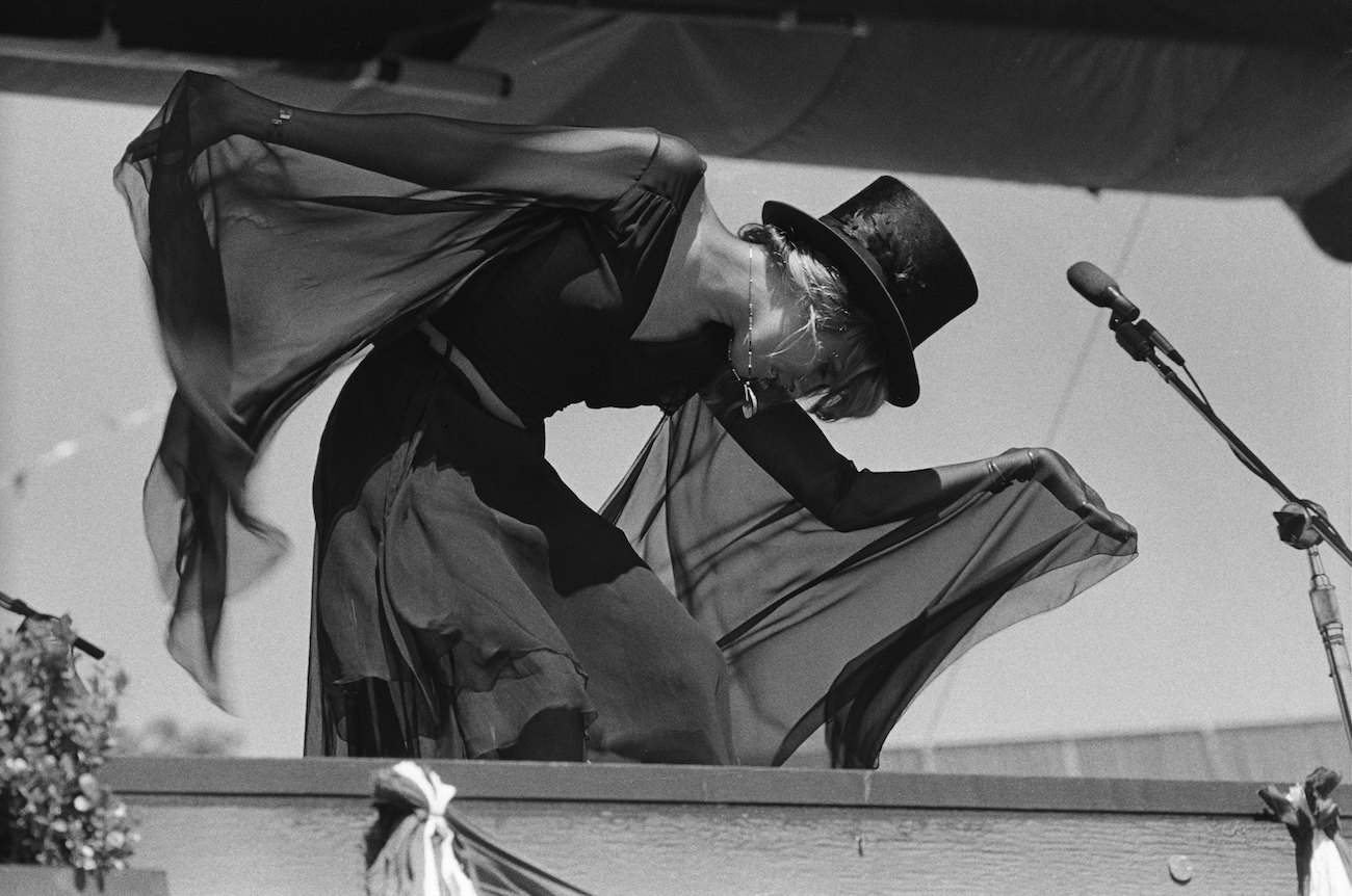 Stevie Nicks bends over, wearing a black outfit and black top hat while performing with Fleetwood Mac in California, 1977.