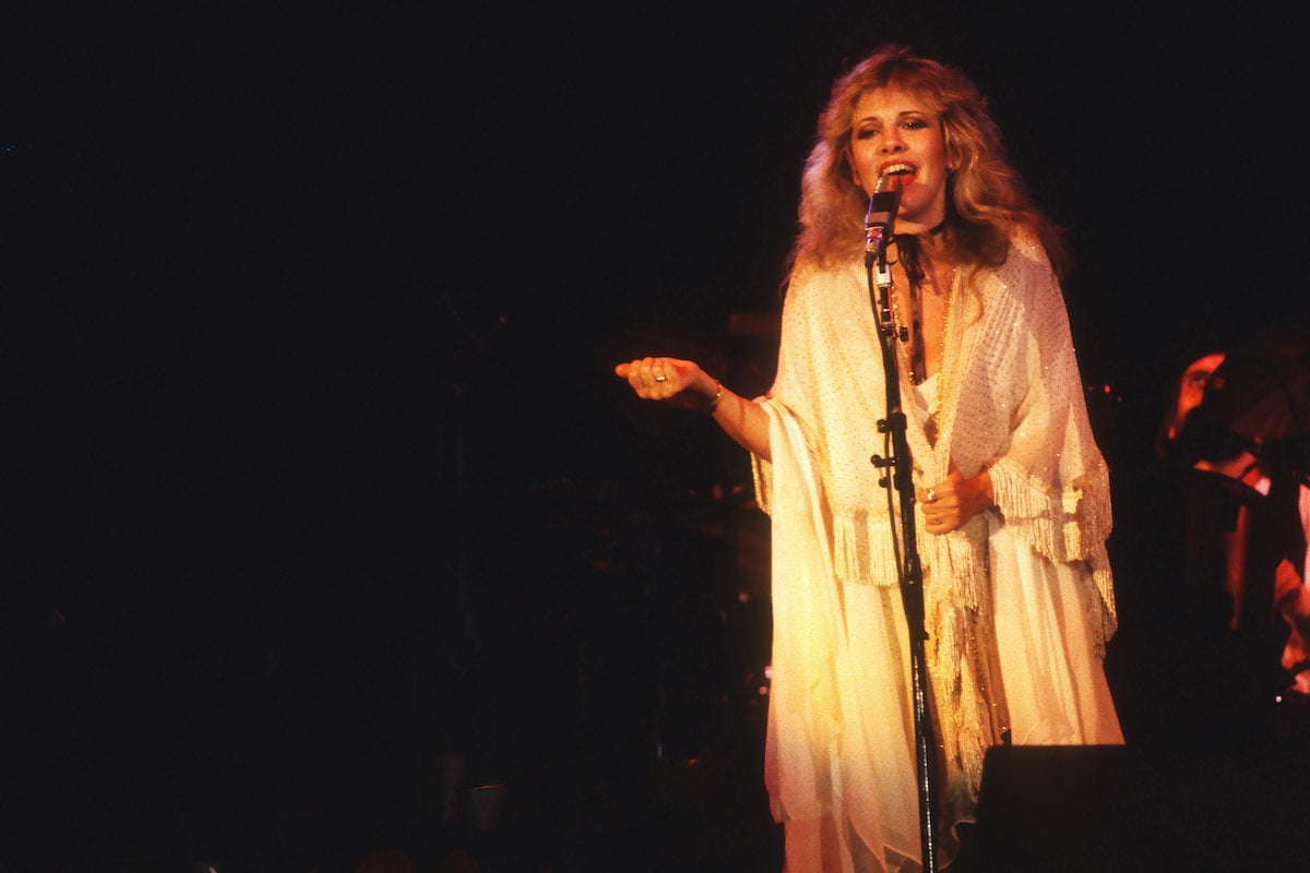 Stevie Nicks performs on stage in a white dress.