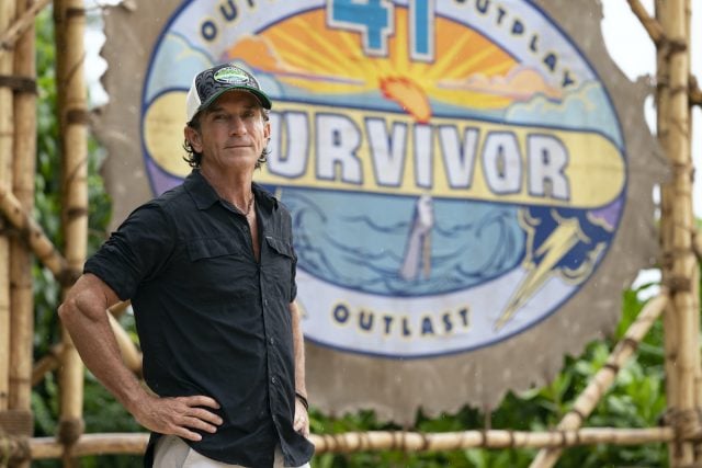 'Survivor' host Jeff Probst stands in front of a 'Survivor' sign
