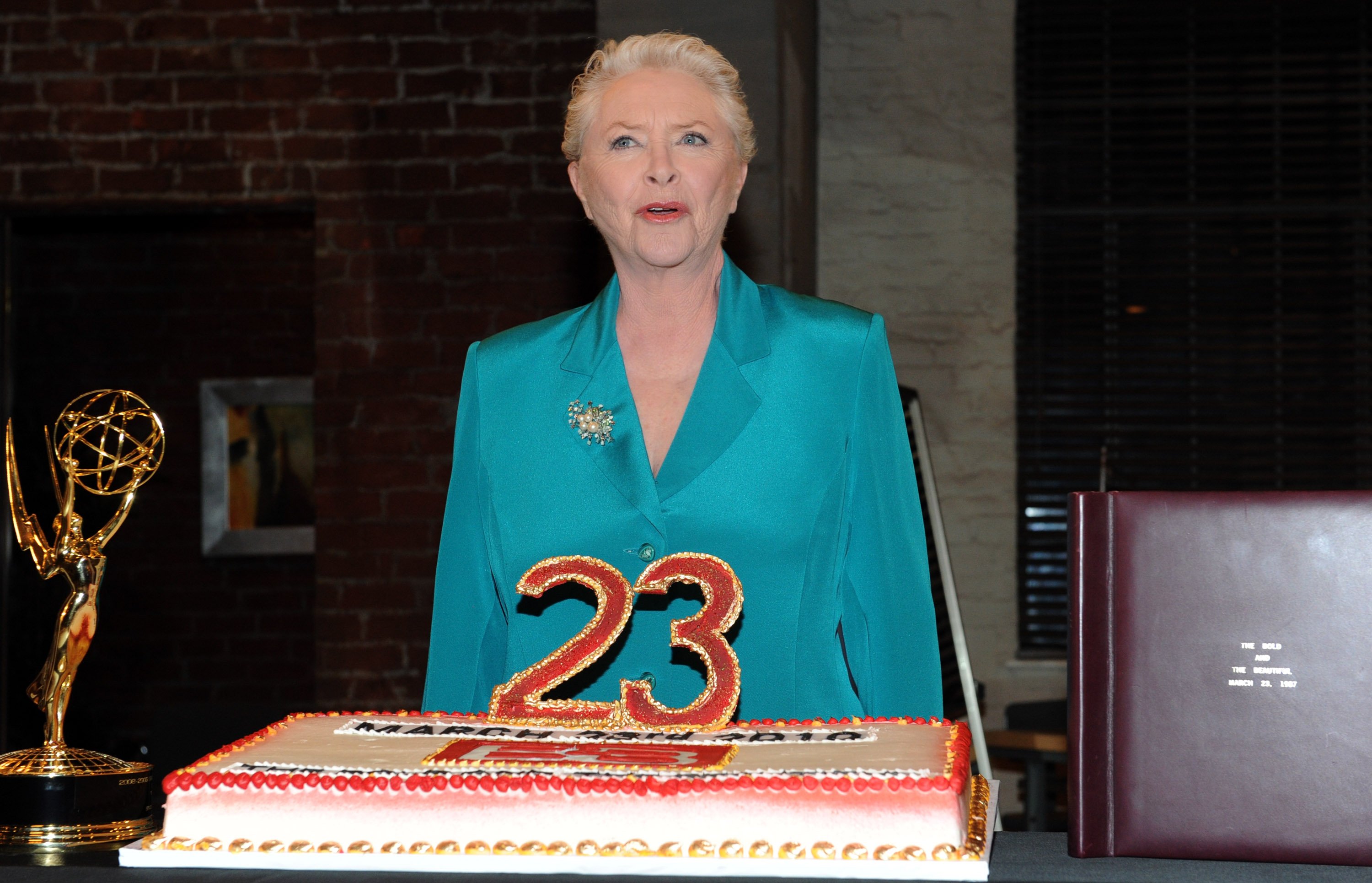 'The Bold and the Beautiful' actor Susan Flannery wearing a blue blouse and standing in front of a cake and Emmy.