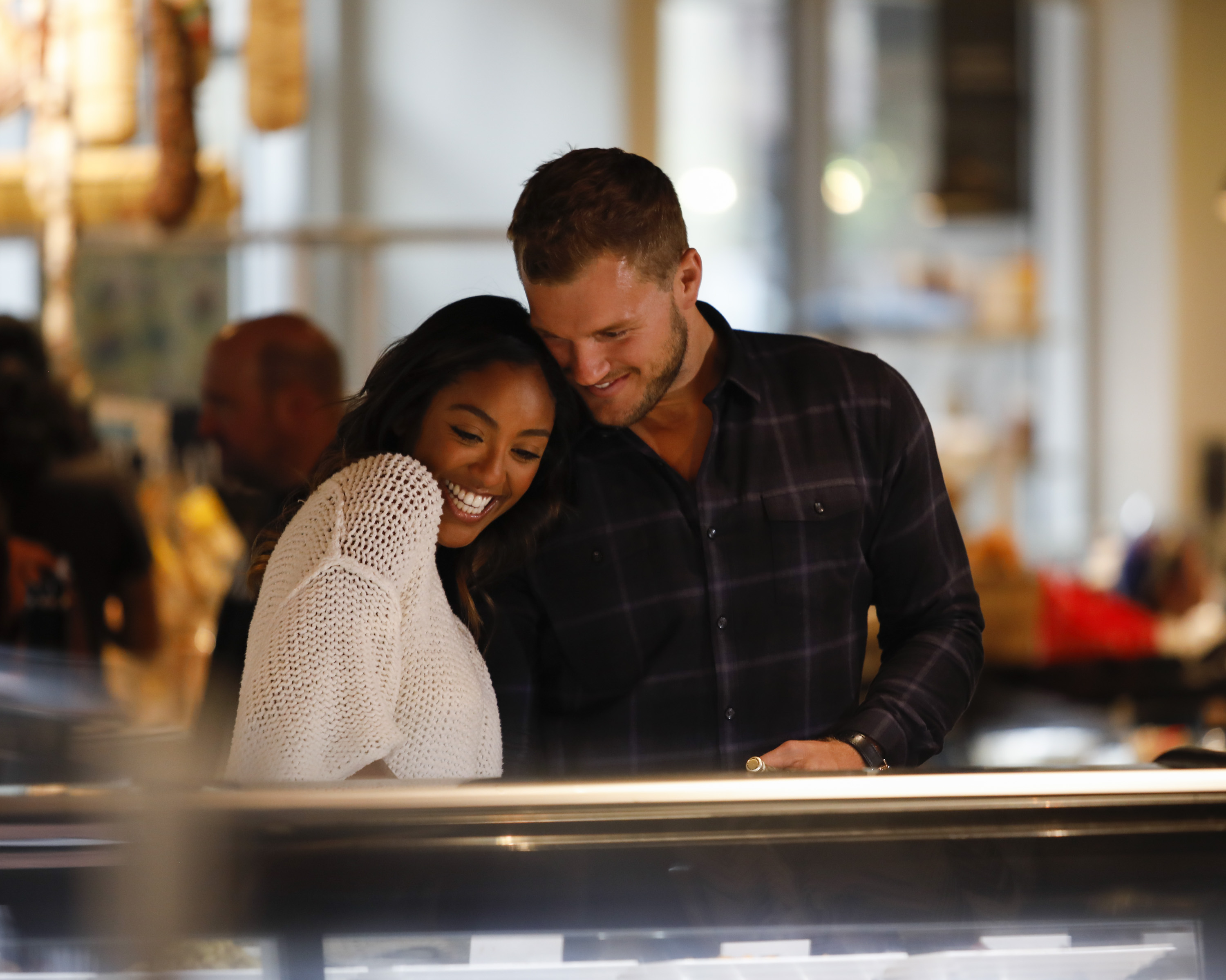 'The Bachelorette' star Tayshia Adams and 'The Bachelor' star Colton Underwood cuddle close. Tayshia wears a white sweater. Colton wears a black and white plaid shirt.