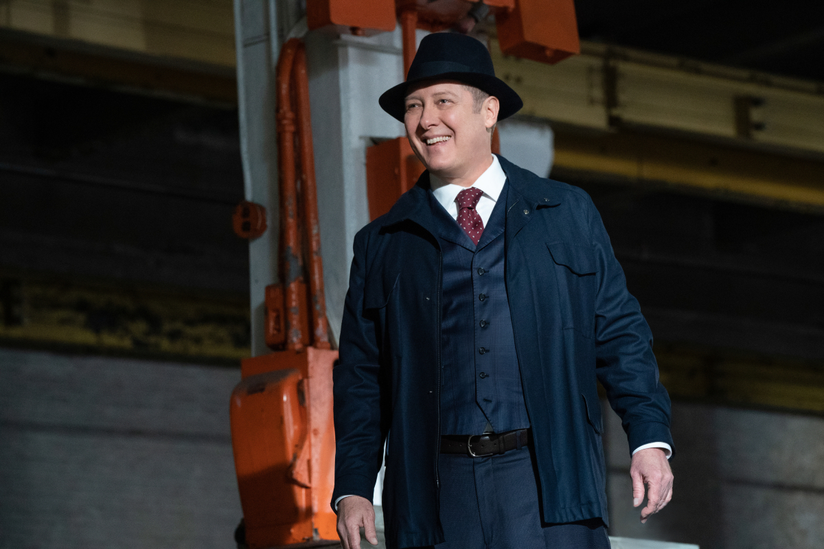 James Spader returns as Raymond "Red" Reddington in The Blacklist Season 9. Red is wearing a suit and hat and smiling. 