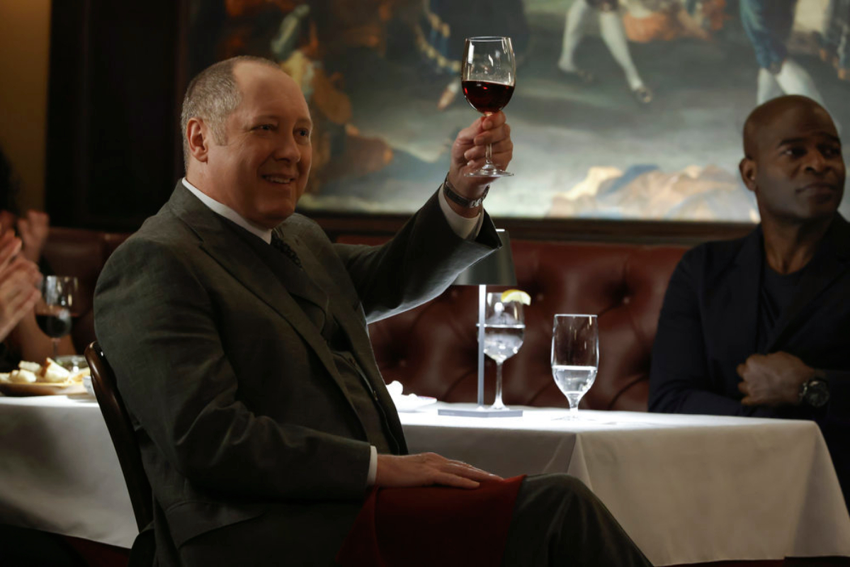 James Spader as Raymond "Red" Reddington and Hisham Tawfiq as Dembe Zuma in The Blacklist. Red smiles and raises a glass of wine for a toast.