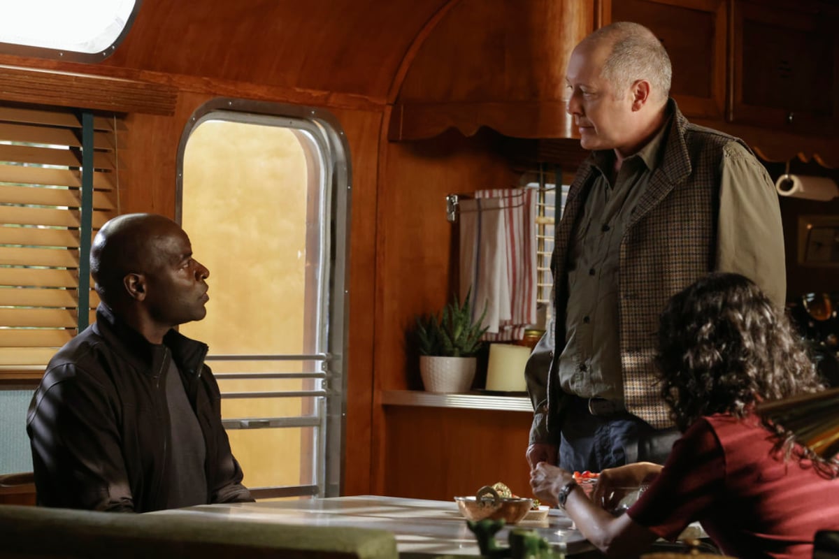 Hisham Tawfiq as Dembe Zuma and James Spader as Red in The Blacklist Season 9 Episode 5. Dembe sits and Red stands in front of him.