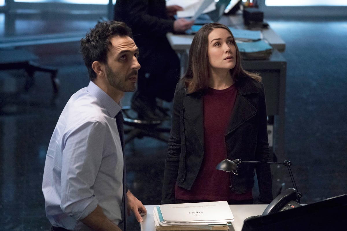 Amir Arison as Aram Mojtabai, Megan Boone as Elizabeth Keen in The Blacklist. Aram and Liz stand at a desk and look up.
