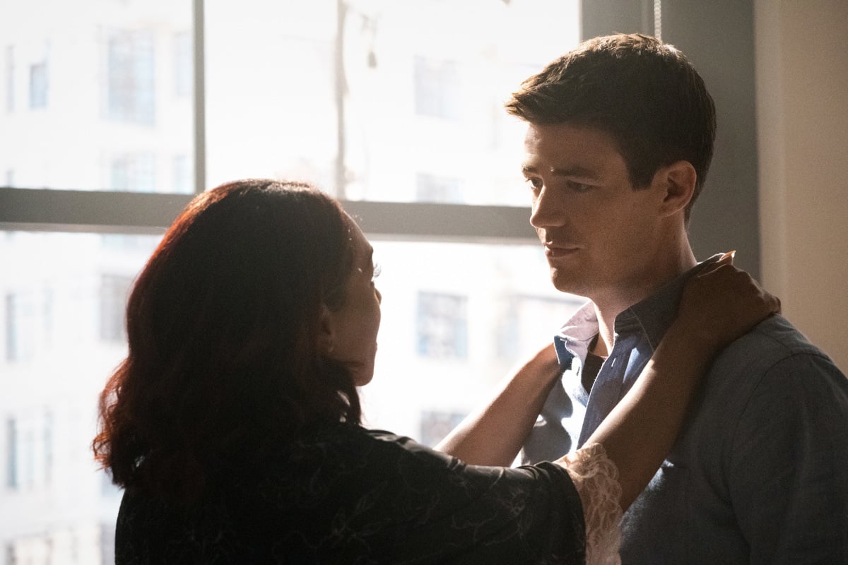 'The Flash' season 8 stars Candice Patton and Grant Gustin, in character as Iris and Barry, stand in front of a window. Iris has her hands on Barry's shoulders as they look at each other. Iris is wearing a black shirt, and Barry is wearing a blue button-up shirt.