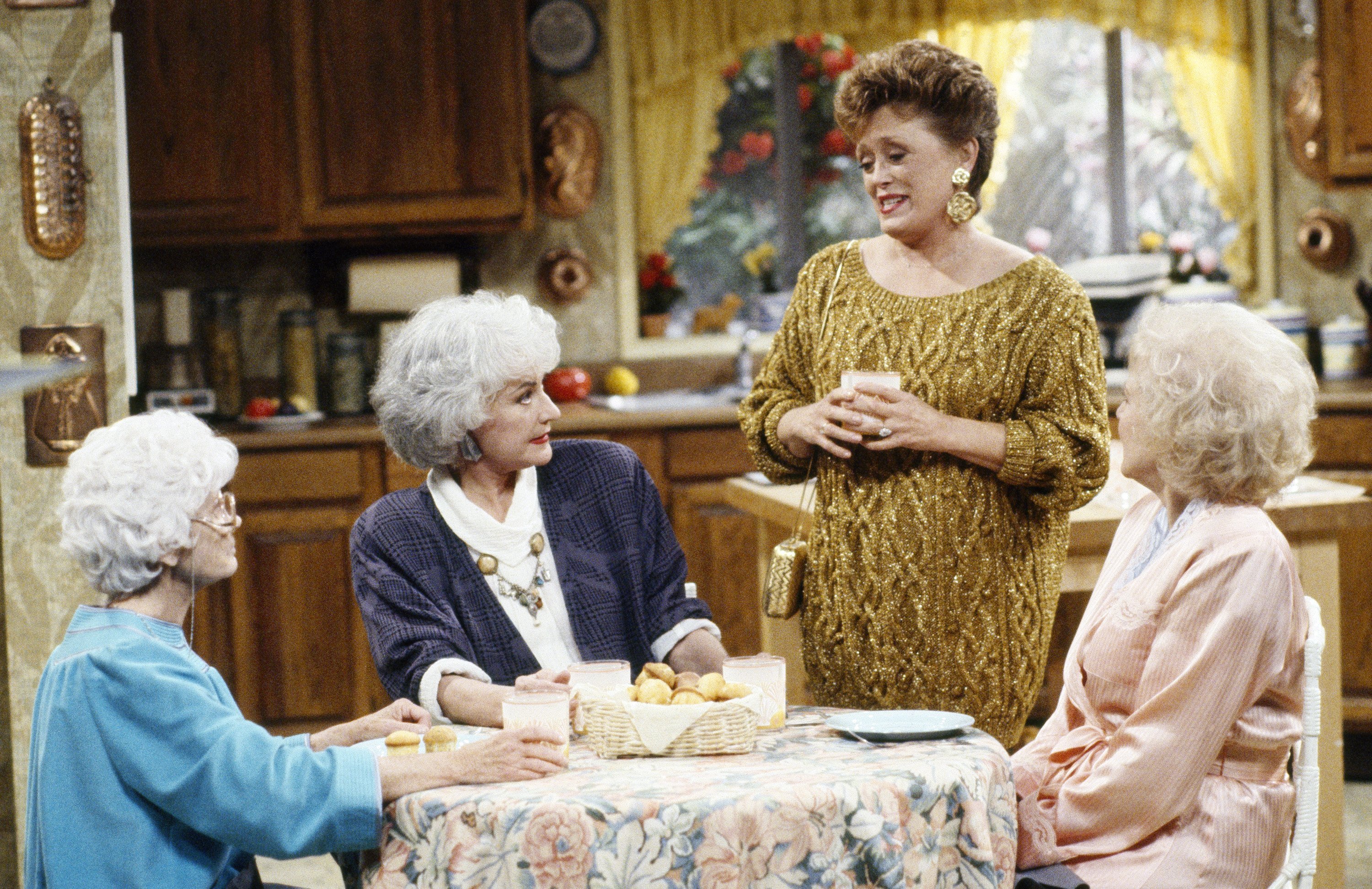 Sophia, Dorothy, and Rose sitting around a kitchen table, with Blanche standing next to them, in an episode of 'The Golden Girls'
