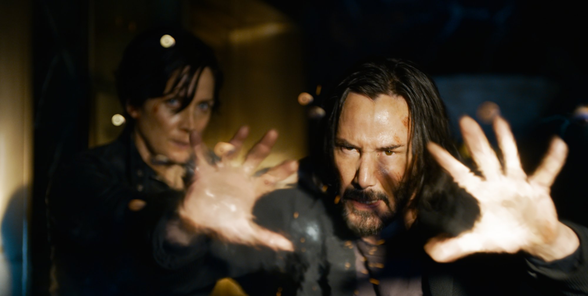 'The Matrix' franchise sequel 'The Matrix Resurrections' actors Carrie-Anne Moss as Trinity and Keanu Reeves as Neo with his hands up