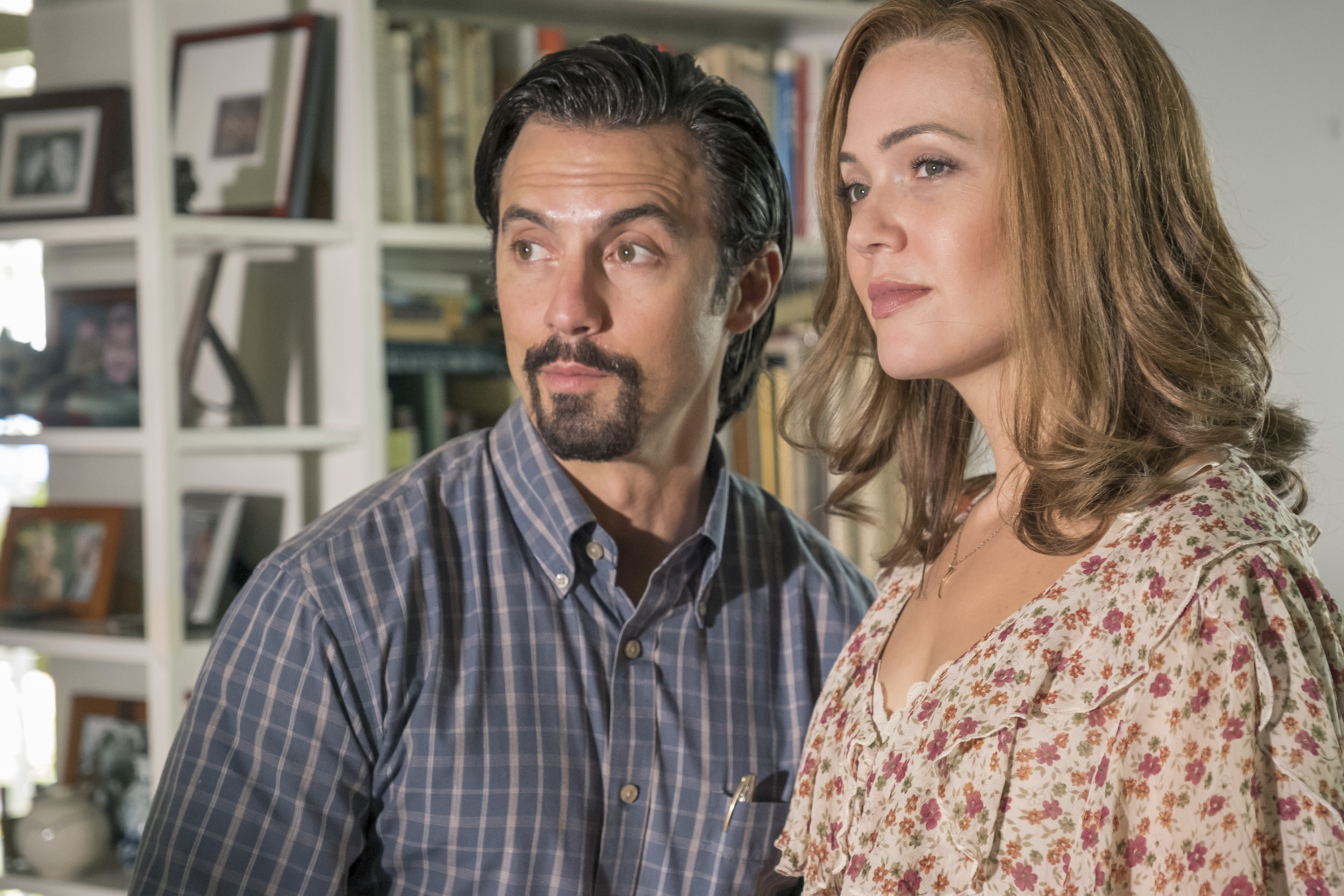 'This Is Us' stars Milo Ventimiglia and Mandy Moore, in character as Jack and Rebecca, stand side-by-side. Ventimiglia wears a blue plaid long-sleeved button-up shirt. Moore wears a white dress with pink and orange flowers on it. Both actors have appeared in 'This Is Us' Thanksgiving episodes.