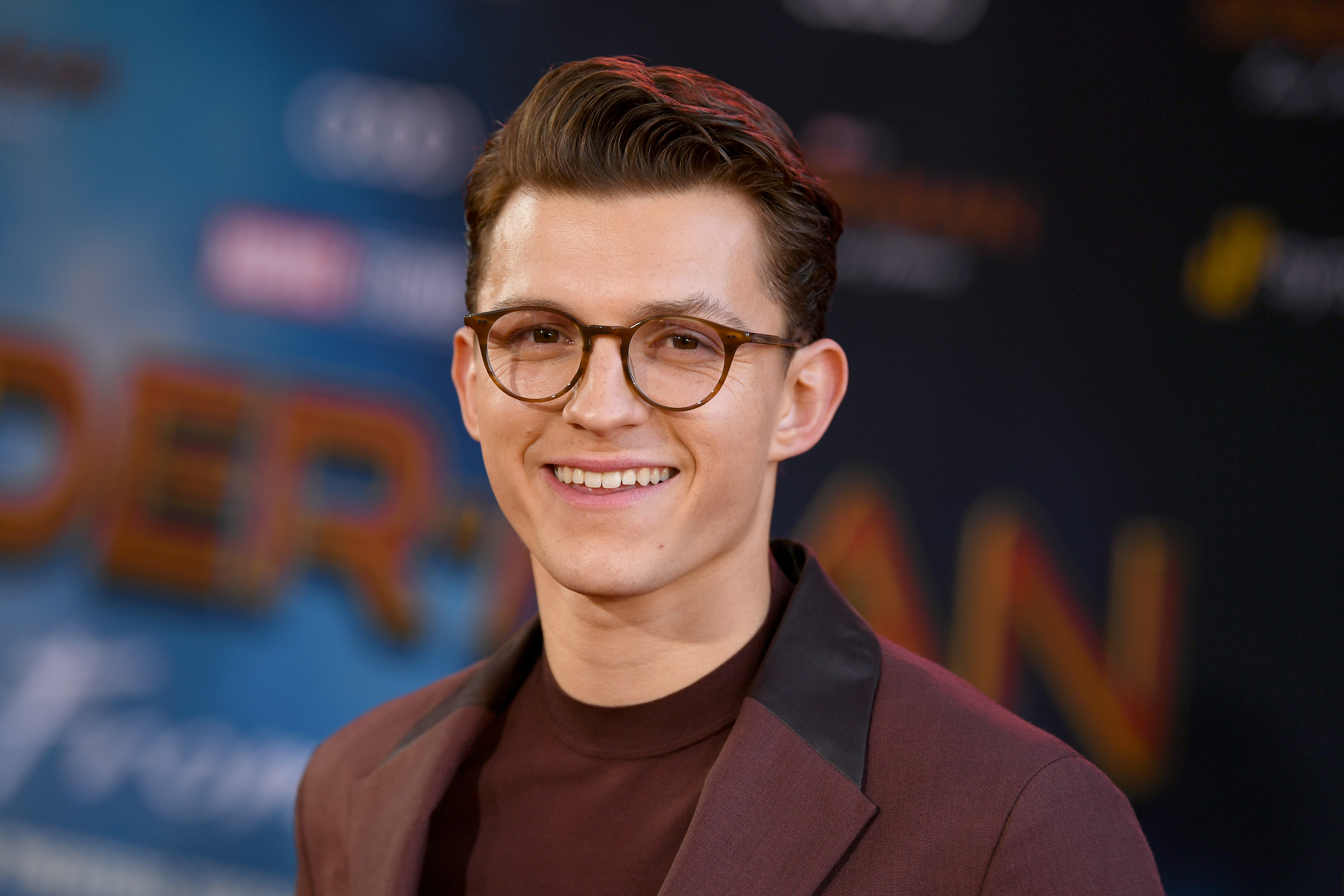 'Spider-Man: No Way Home' star Tom Holland wears a maroon suit over a maroon shirt and glasses.