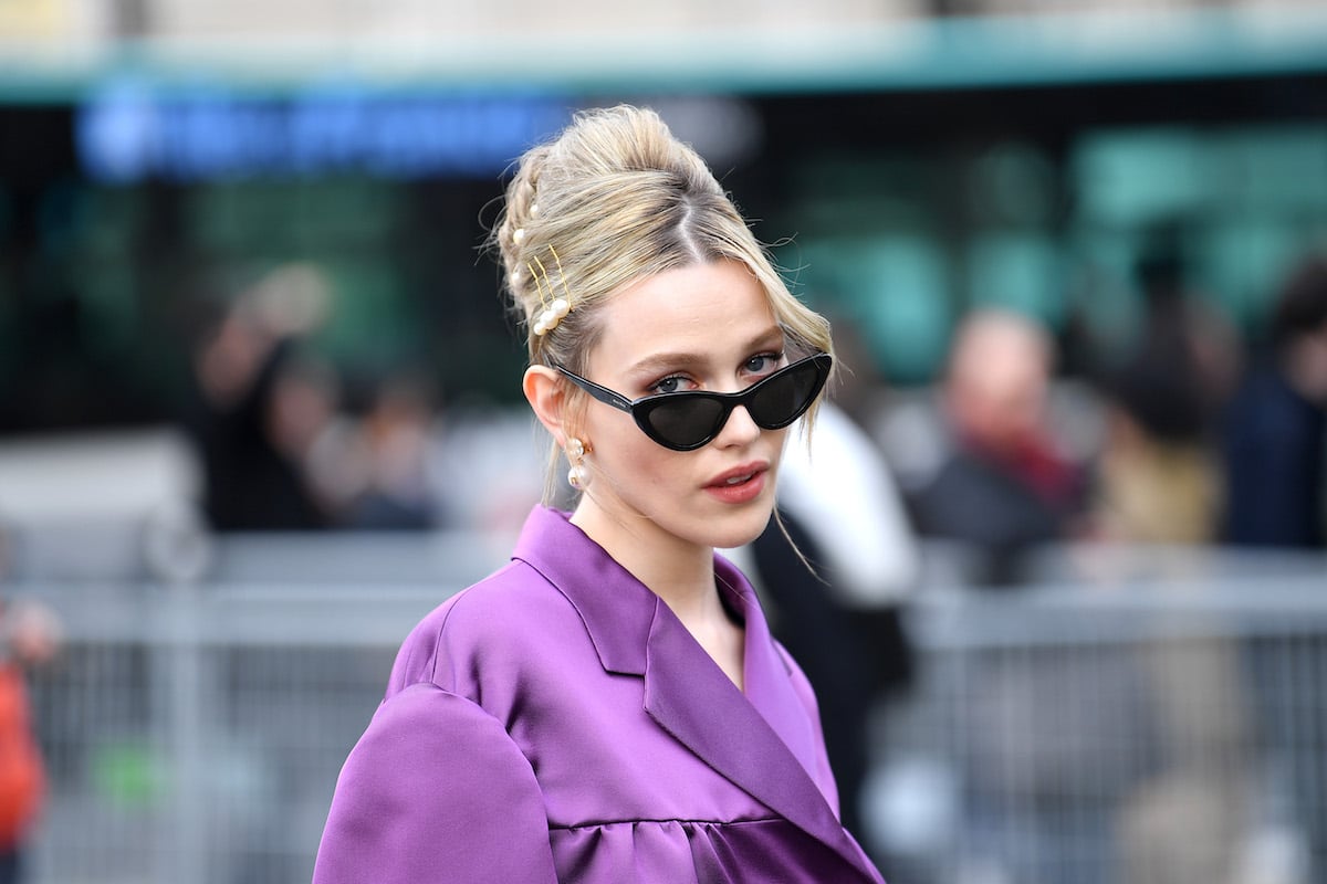 Victoria Pedretti peeks over the top of her sunglasses at the camera.