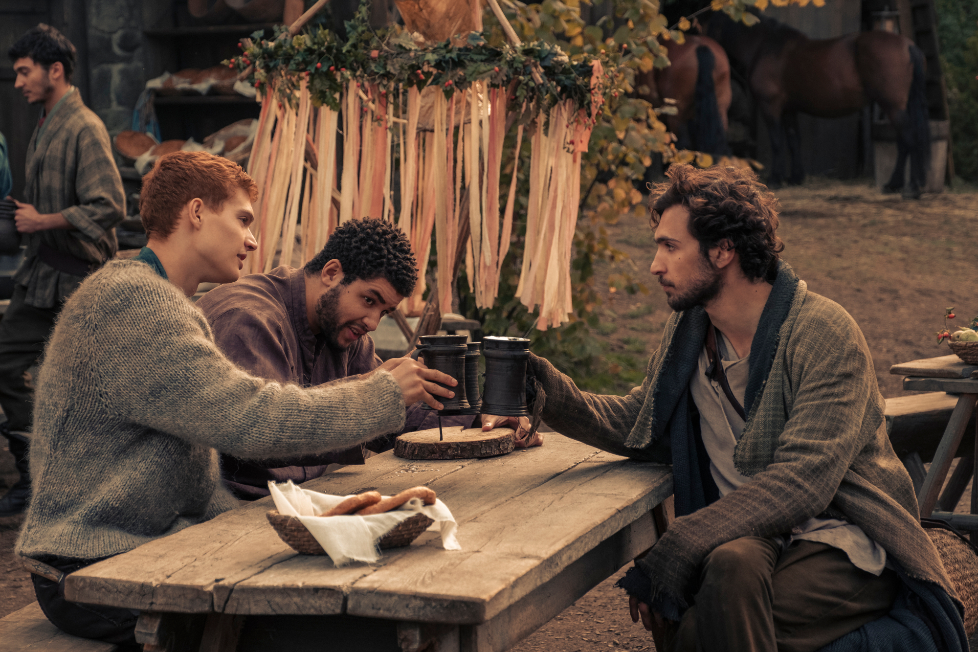 Josha Stradowski (Rand al’Thor), Marcus Rutherford (Perrin Aybara), and Barney Harris (Mat Cauthon) in Amazon Prime Video's 'The Wheel of Time' series, based on the best-selling books by Robert Jordan. The three are sitting around a table and drinking.