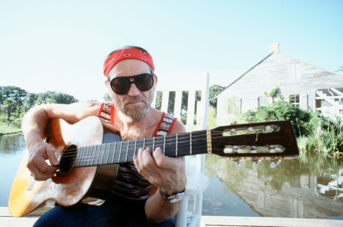 Willie Nelson plays his guitar, wearing sunglasses and a headband c. 1978