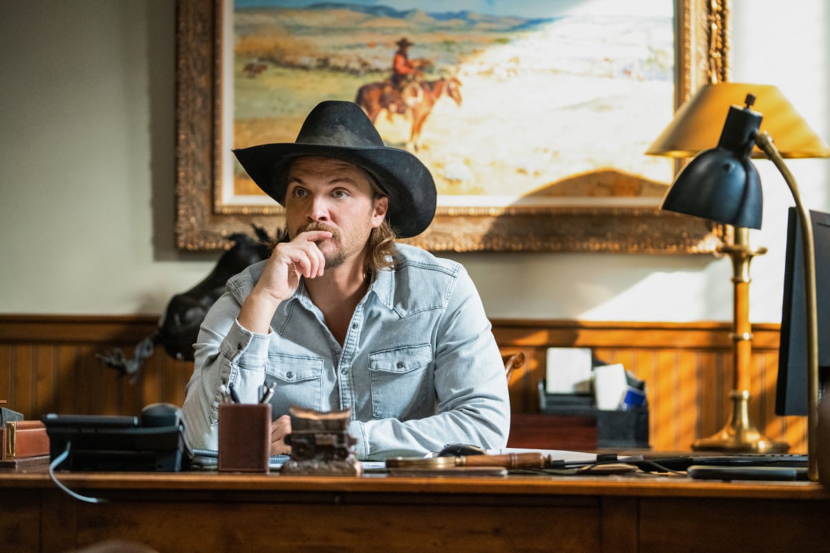 Luke Grimes as Kayce Dutton in Yellowstone. Kayce sits at his desk wearing a cowboy hat.