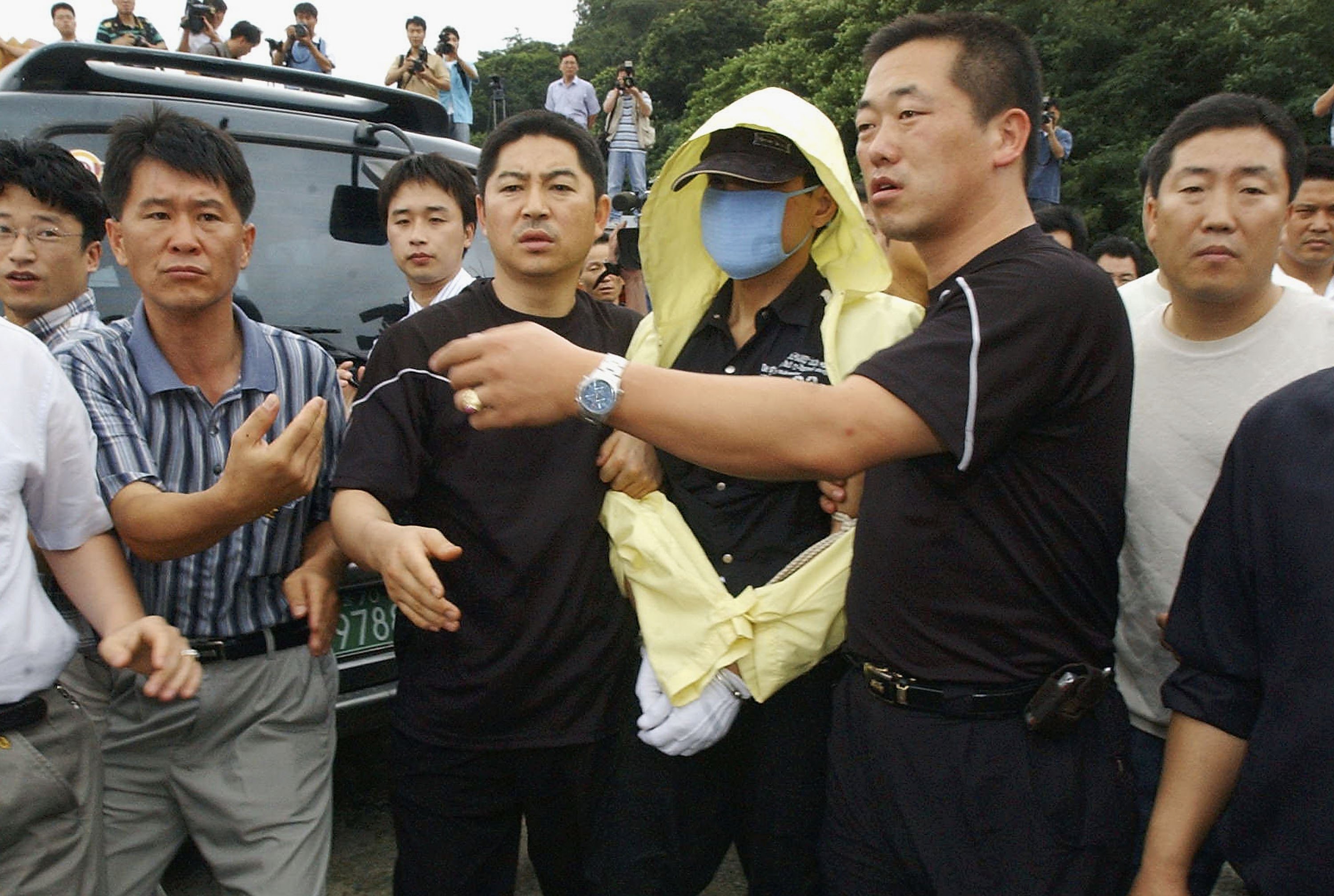 Yoo Young-chul after his arrest being held by police wearing a yellow coat.