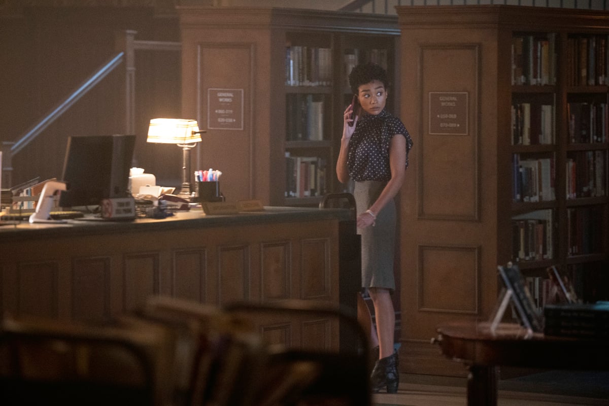 Tati Gabrielle may return to her role as Marienne in You Season 4. She stands in the library on the phone looking over her shoulder. 