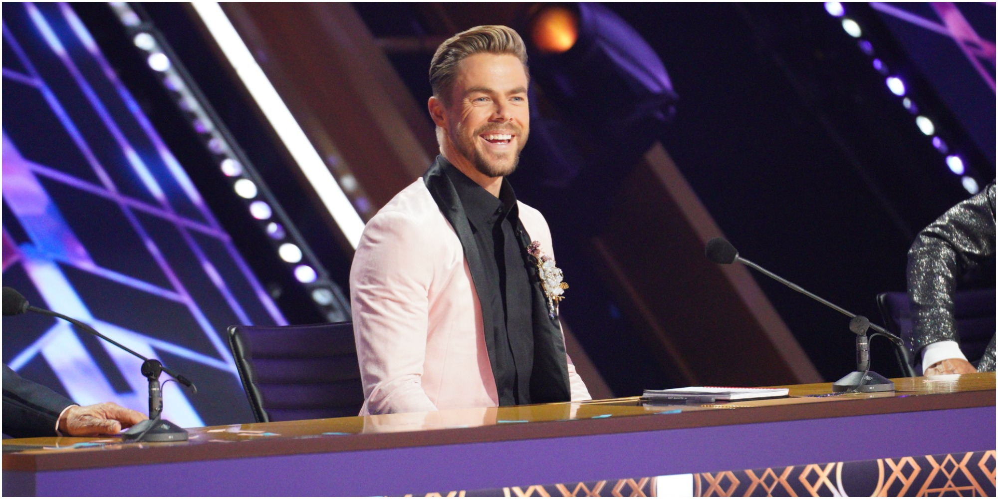 Derek Hough is seated behind the judges table on the set of "Dancing with the Stars."
