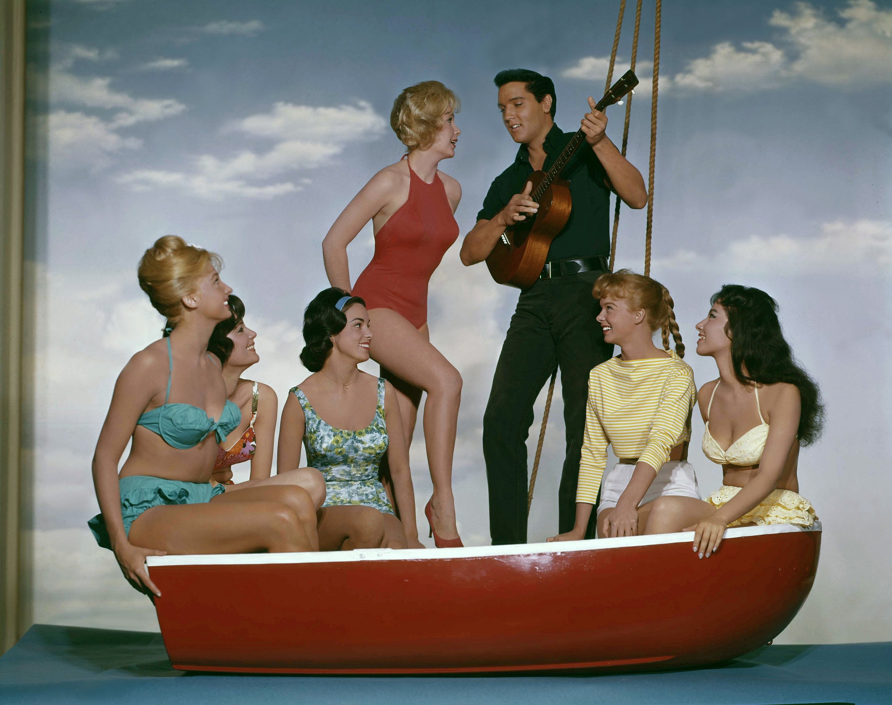 Elvis Presley strumming his guitar on a boat surrounded by other actors