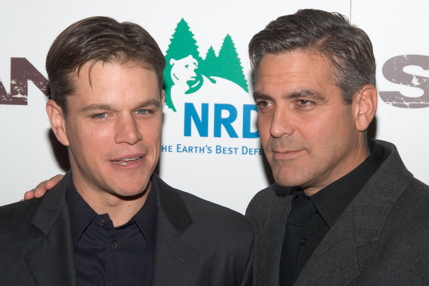 Matt Damon smiles and George Clooney stands by looking serious on the red carpet of 'Syriana' premiere.