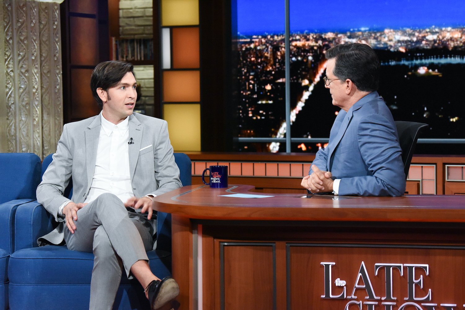 Nicholas Braun wears a light colored suit and white shirt during a 2019 interview on 'The Late Show with Stephen Colbert'