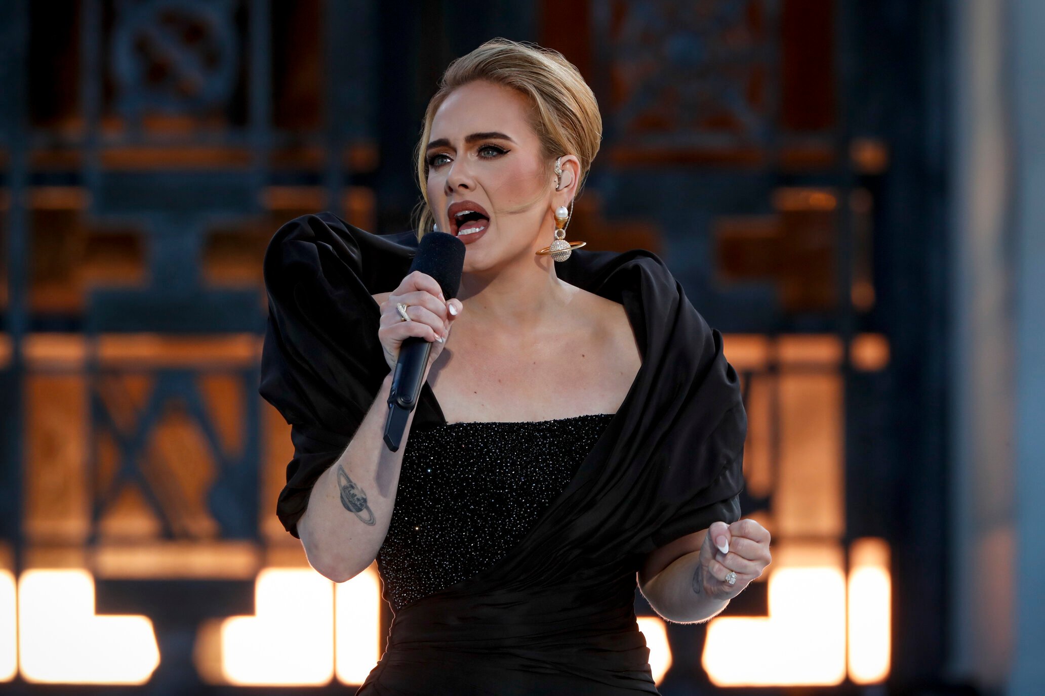 Adele singing into a microphone in a black dress.