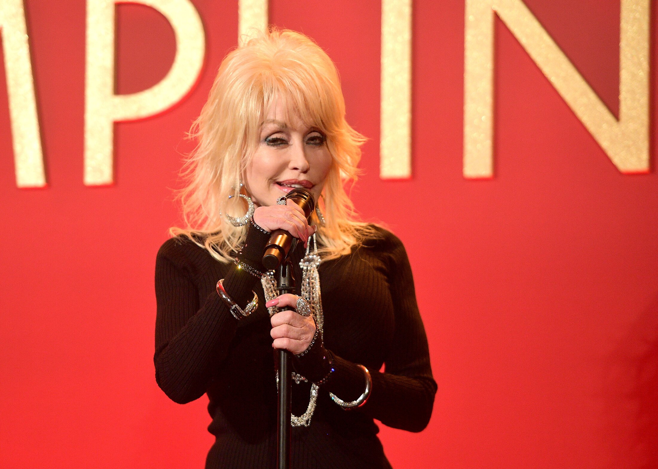 Dolly Parton performs onstage wearing a black outfit in 2018
