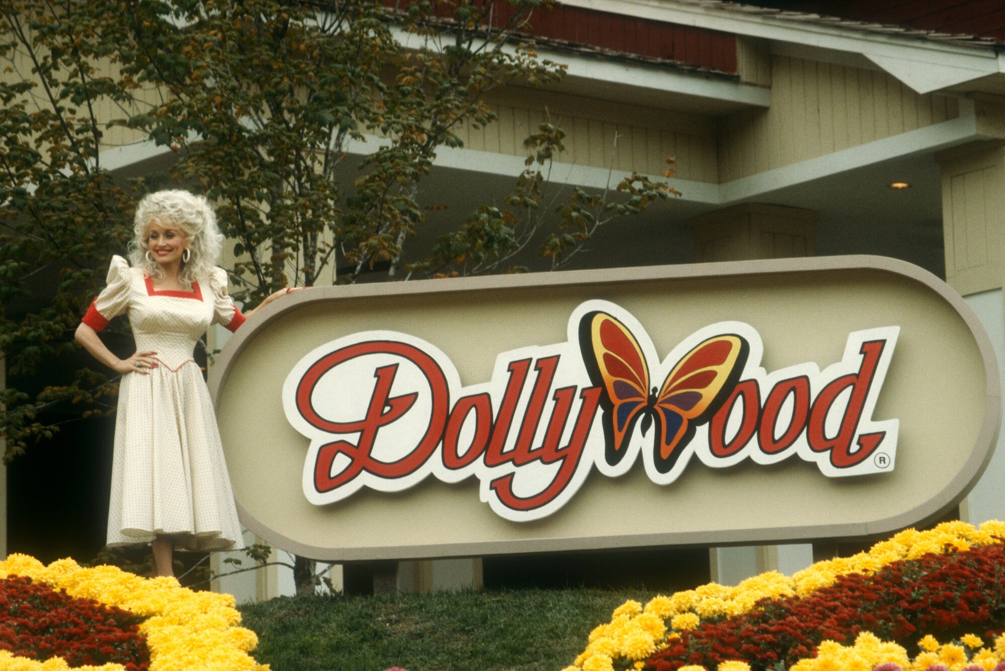 Dolly Parton standing in front of the 'Dollywood' sign at Dollywood