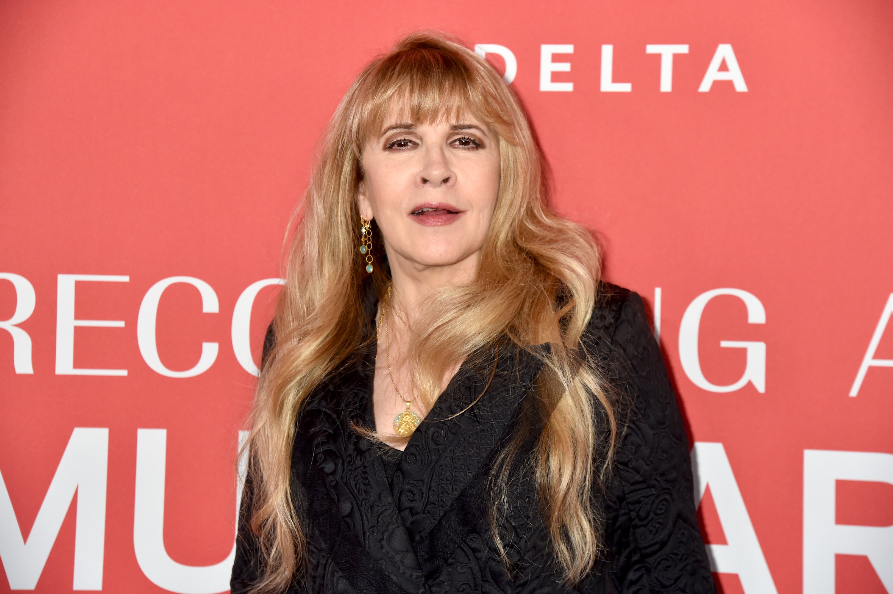Stevie Nicks poses in front of a red wall.