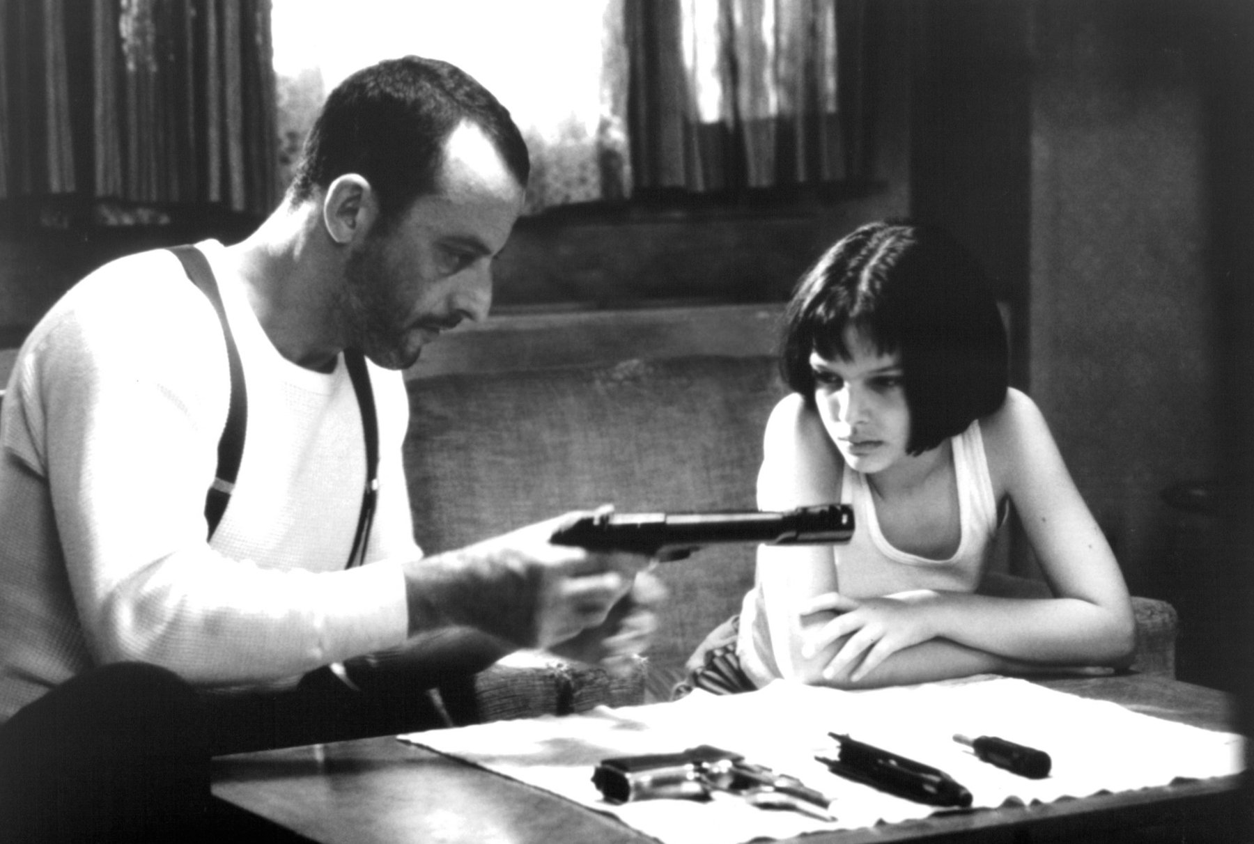 Jean Reno loads a gun in front of Natalie Portman in a scene from the film 'Léon: The Professional', 1994