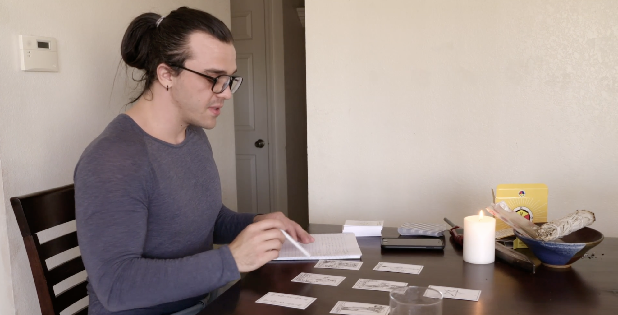 'Before the 90 Days' Season 5 star Caleb sitting at a table with tarot cards in front of him while wearing a long sleeved gray shirt.