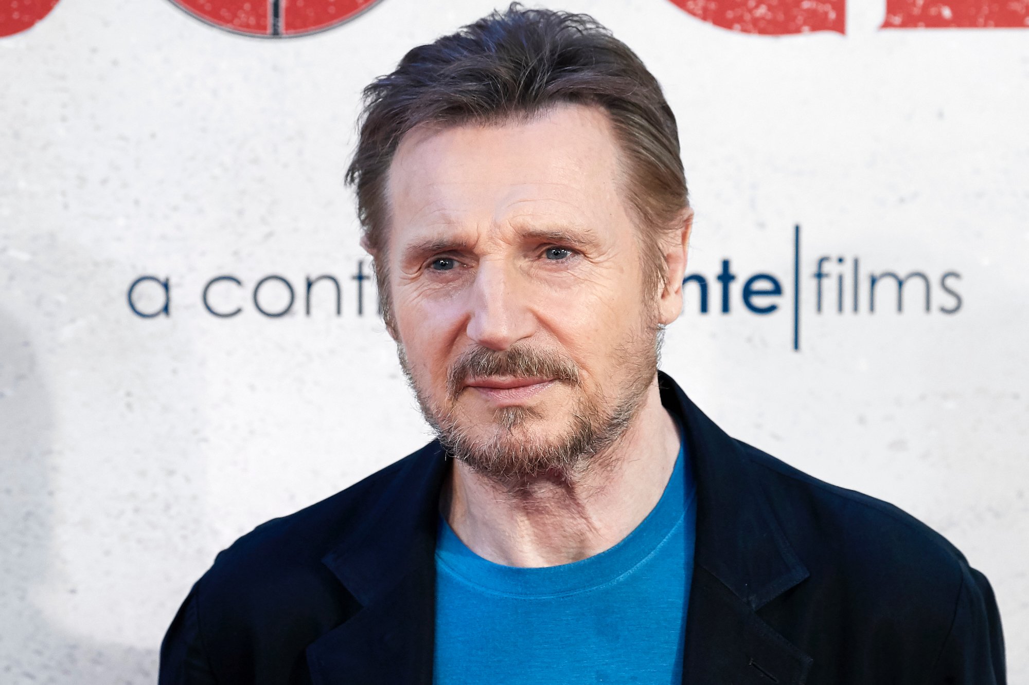 'A Million Ways to Die in the West' actor Liam Neeson with a blue shirt in front of a step and repeat
