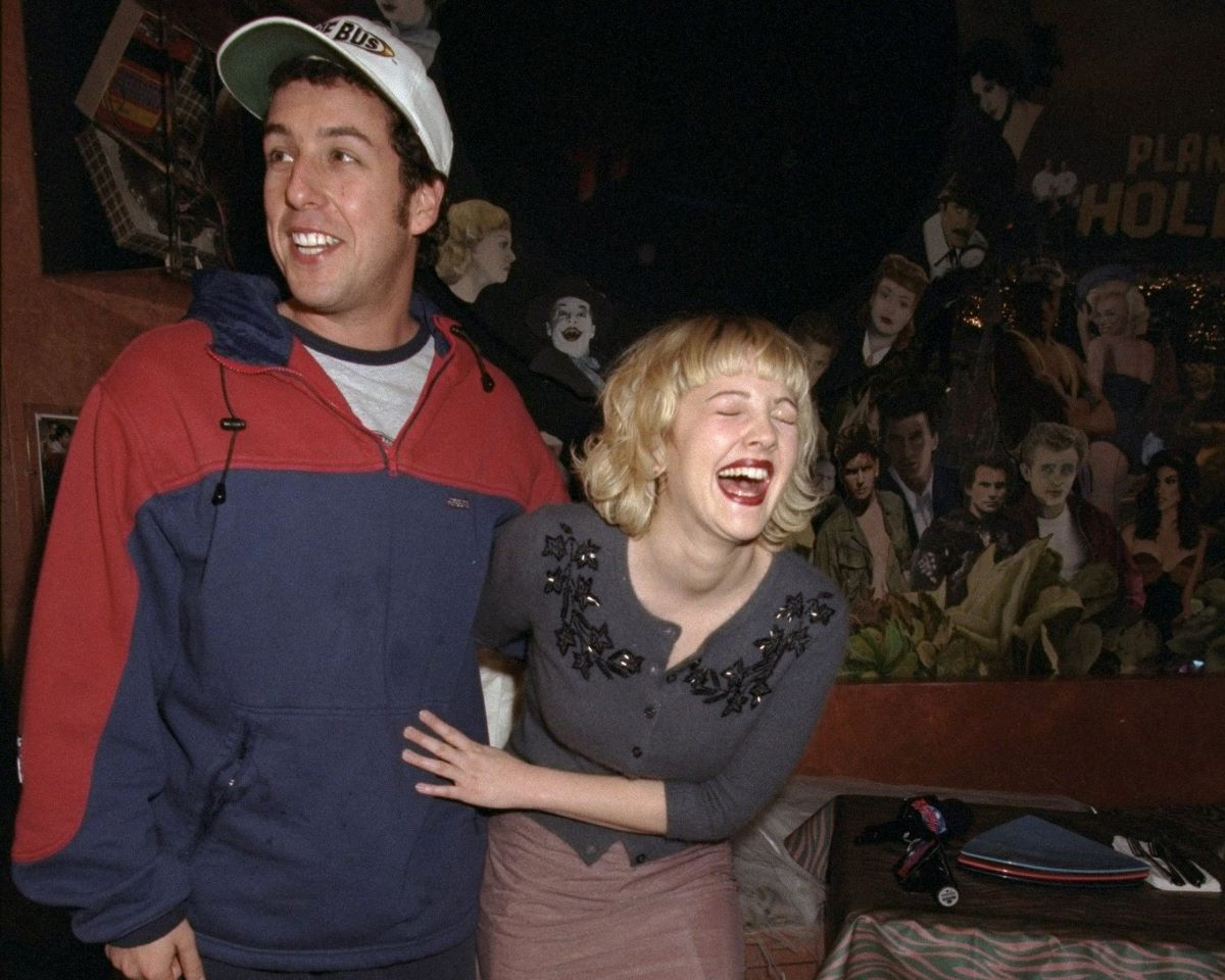 Adam Sandler wearing a baseball cap and posing with a laughing Drew Barrymore