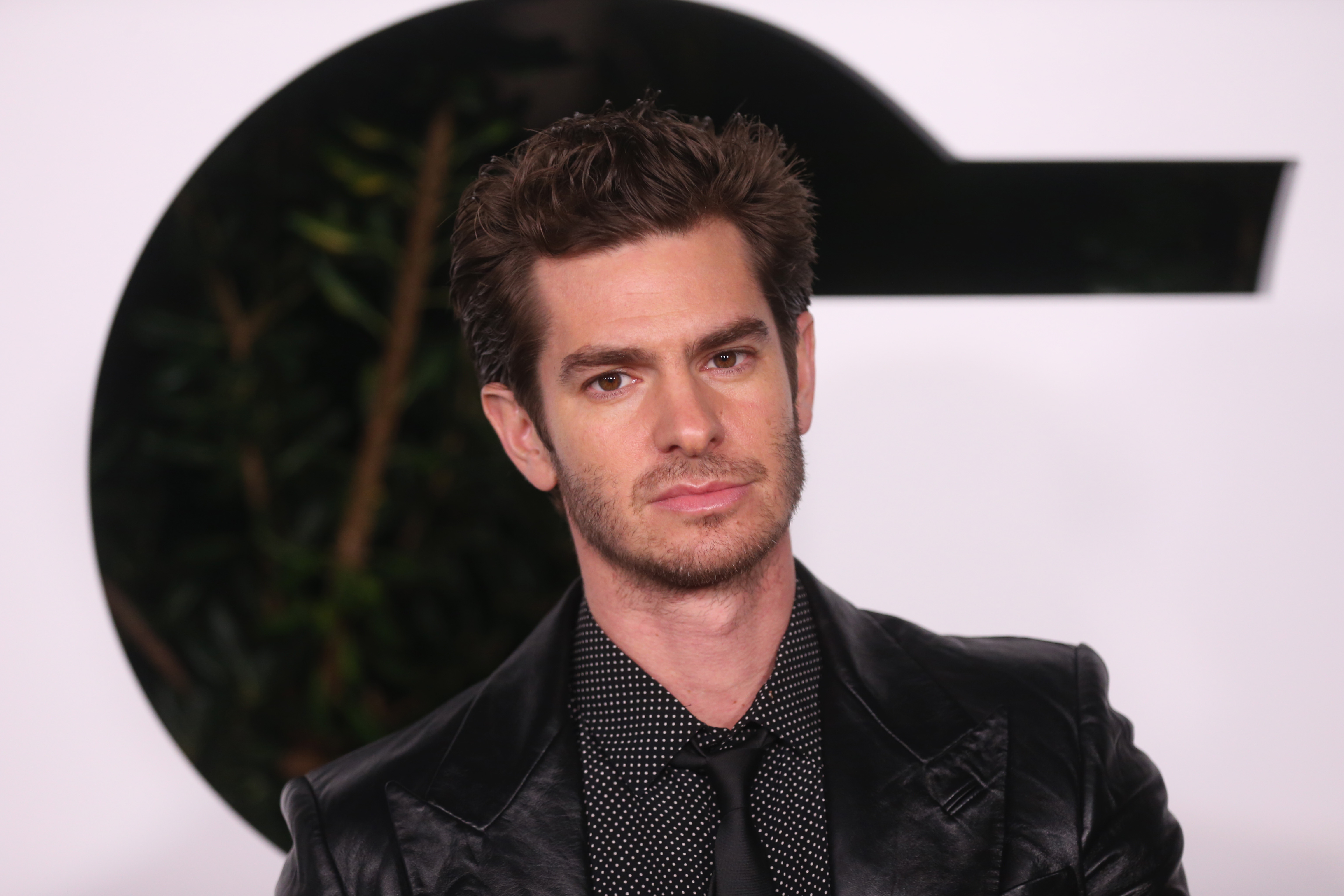 'Spider-Man: No Way Home' and 'The Amazing Spider-Man' star Andrew Garfield wears a black leather jacket over a black button-up shirt with white polka dots and a black tie.