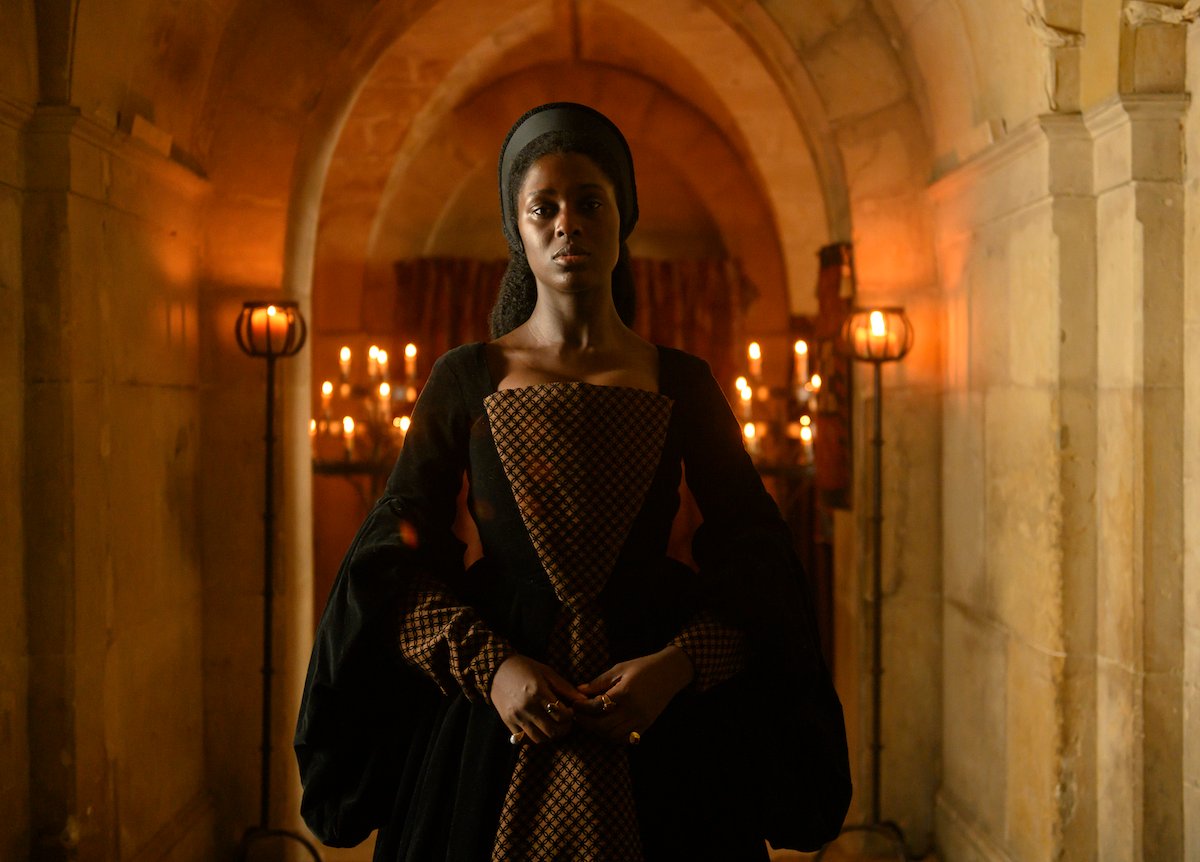 Jodie Turner-Smith as Anne Boleyn, wearing a black dress and standing in a candlelit hallway