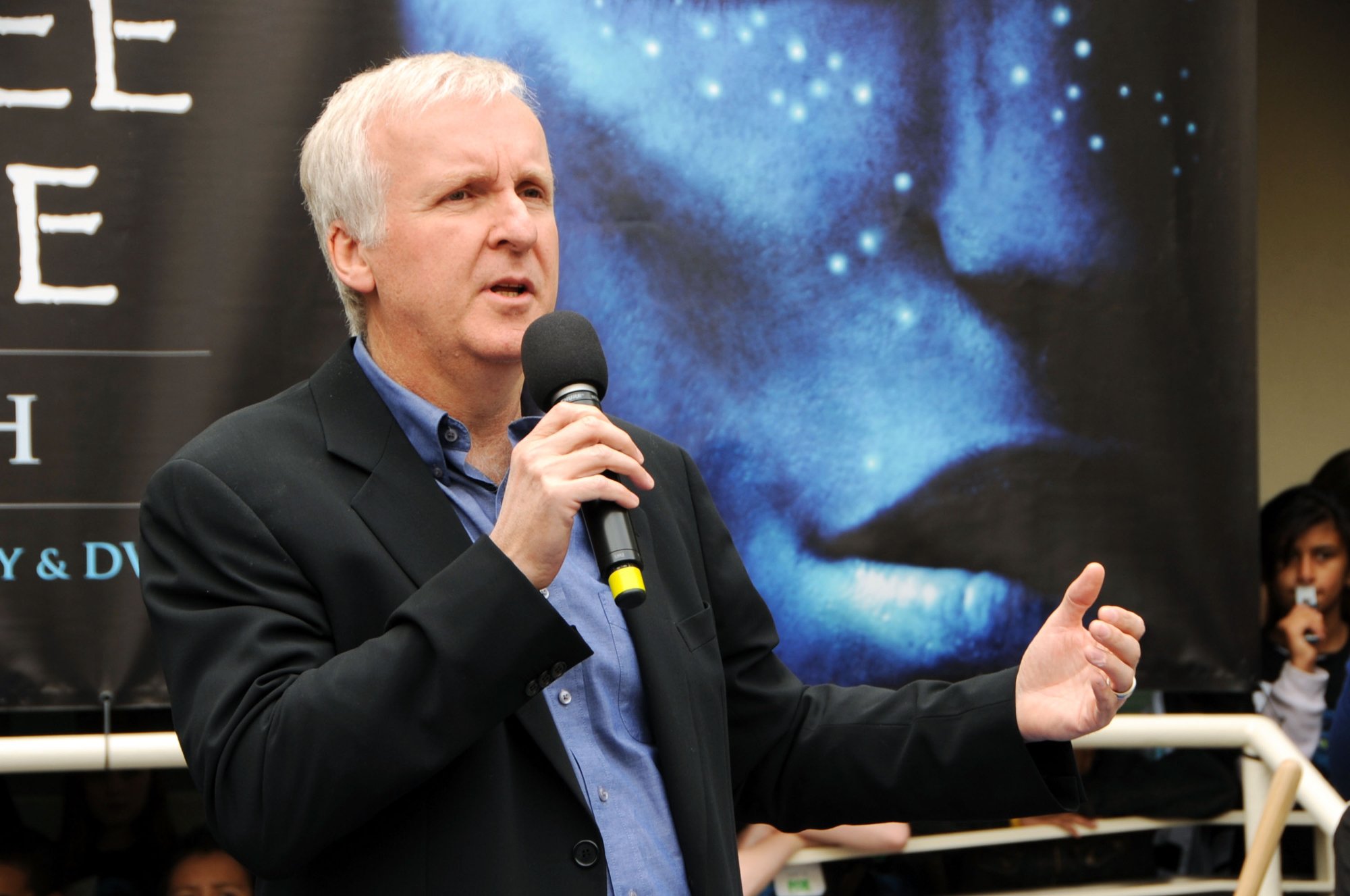 'Avatar' sequels filmmaker James Cameron speaking into a mic in front of an 'Avatar' banner