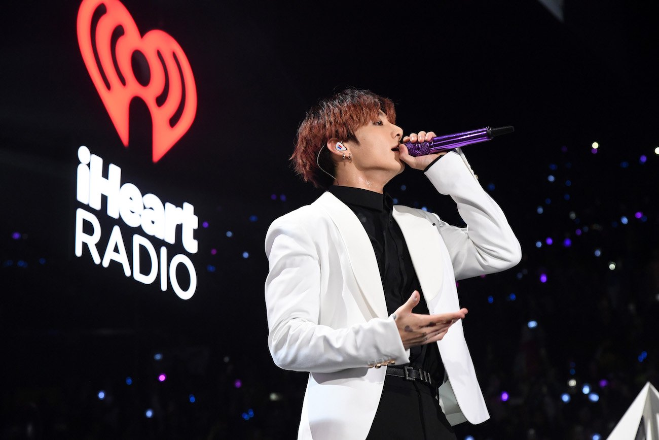 Jungkook singing into a microphone, wearing a white jacket
