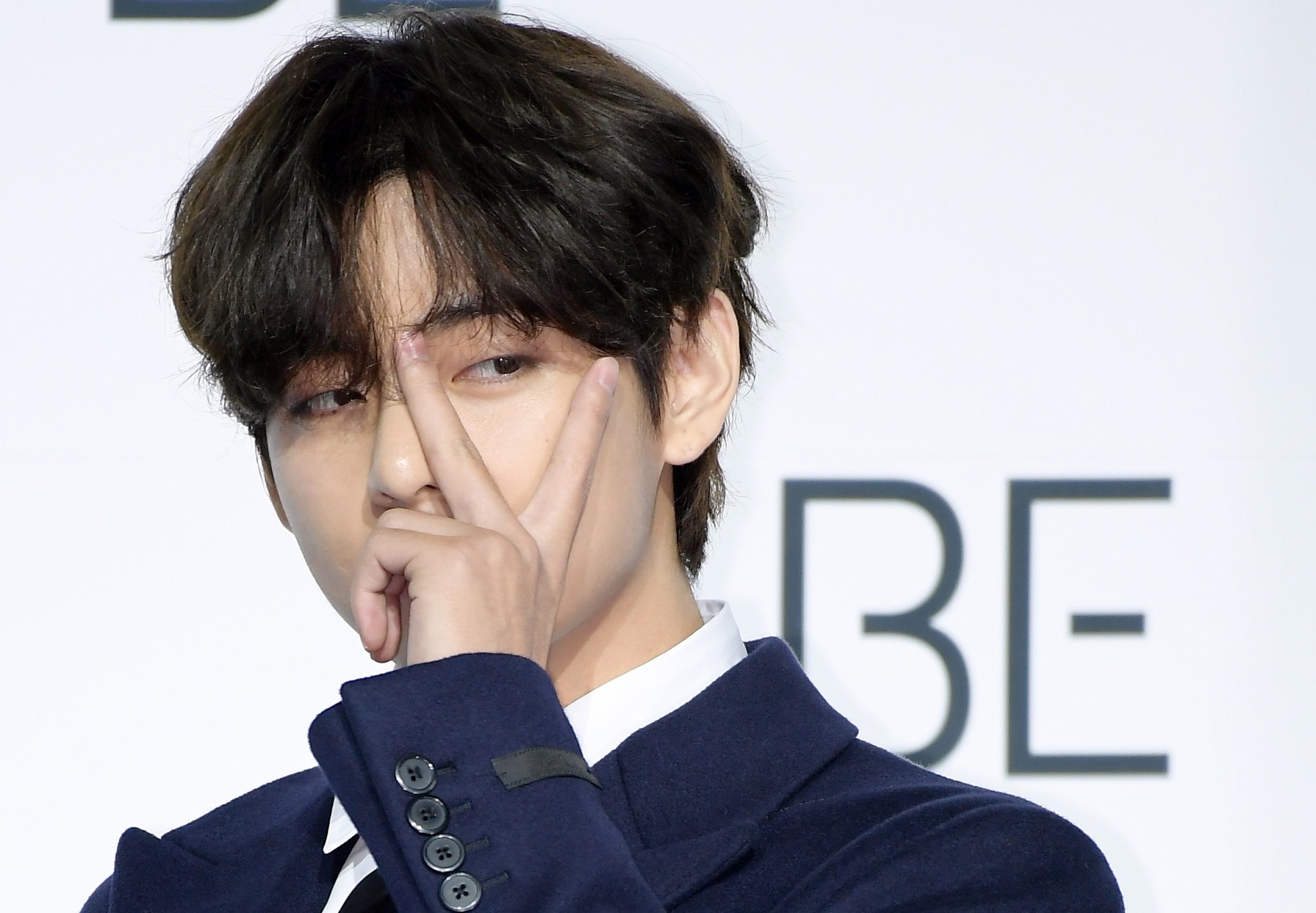 V of BTS covers his face with the peace sign at BTS' 'BE' album press conference