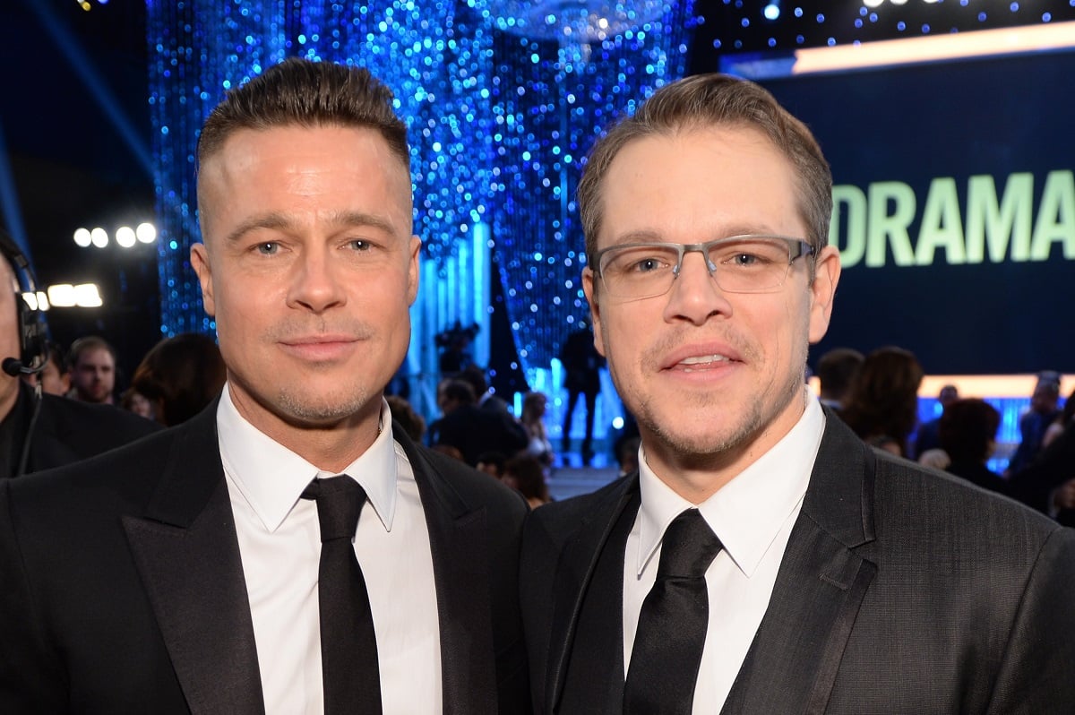 Brad Pitt and Matt Damon smiling while wearing business suits.
