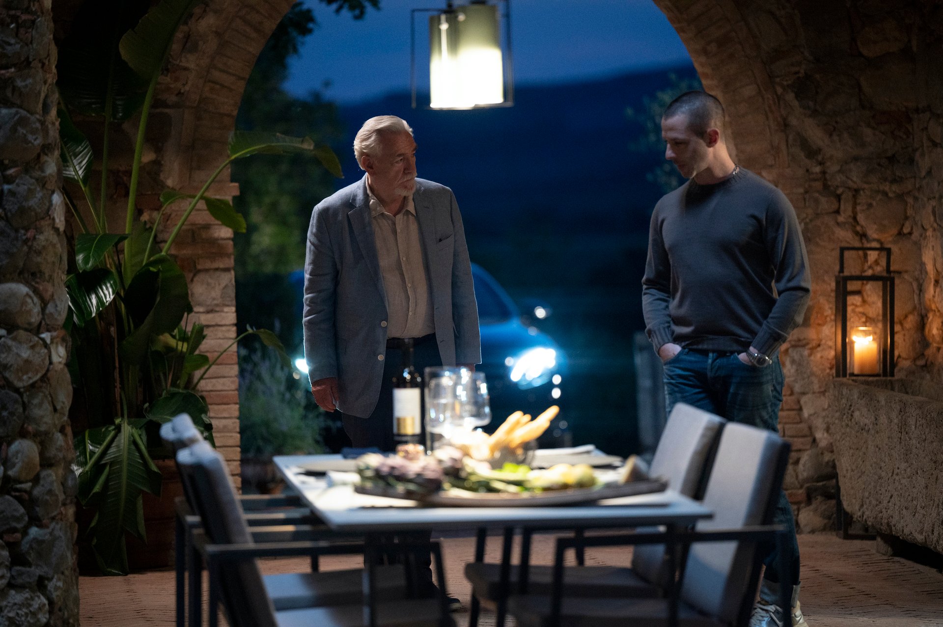 Brian Cox and Jeremy Strong as Logan and Kendall Roy in 'Succession' Season 3 Episode 8. The two are standing near a dinner table, and neither of them looks happy.