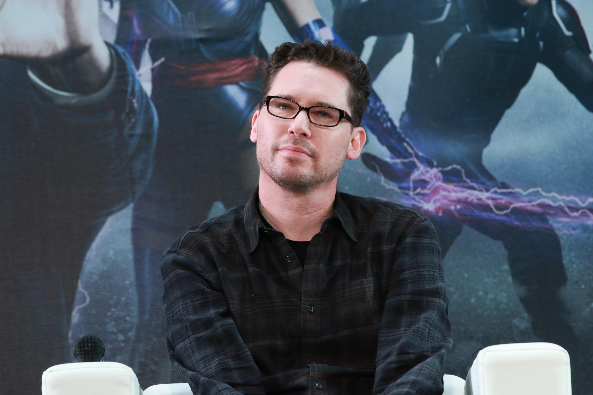 Bryan Singer in article about abuse wearing glasses in front of an 'X-Men' poster
