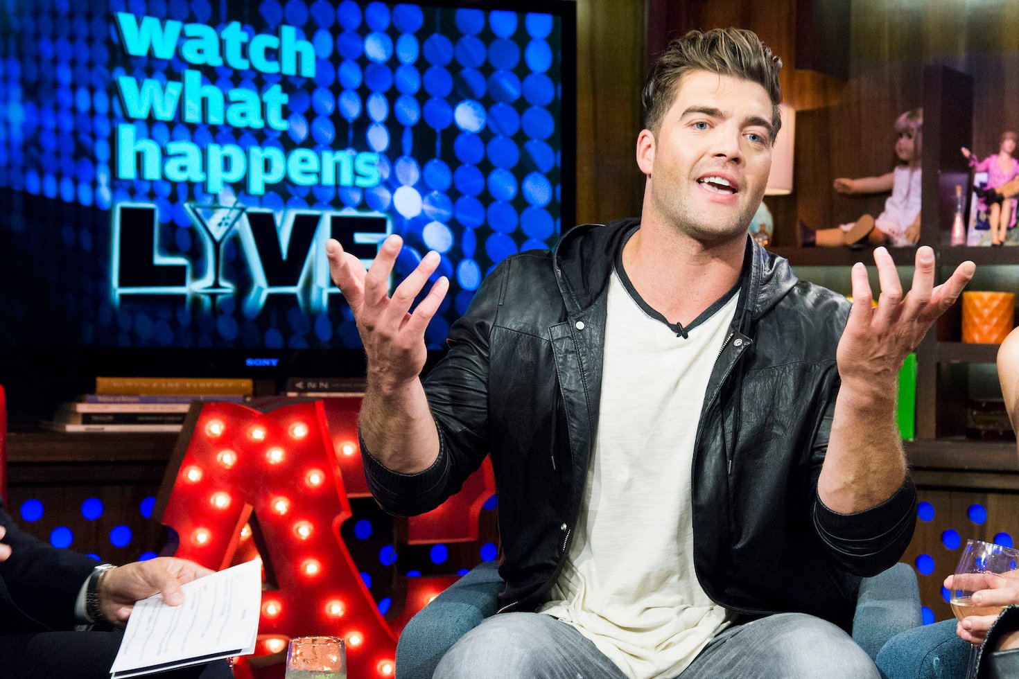 CT Tamburello, 'The Challenge' Season 37 winner, sitting on a couch in a leather jacket with his hands up on 'Watch What Happens Live'