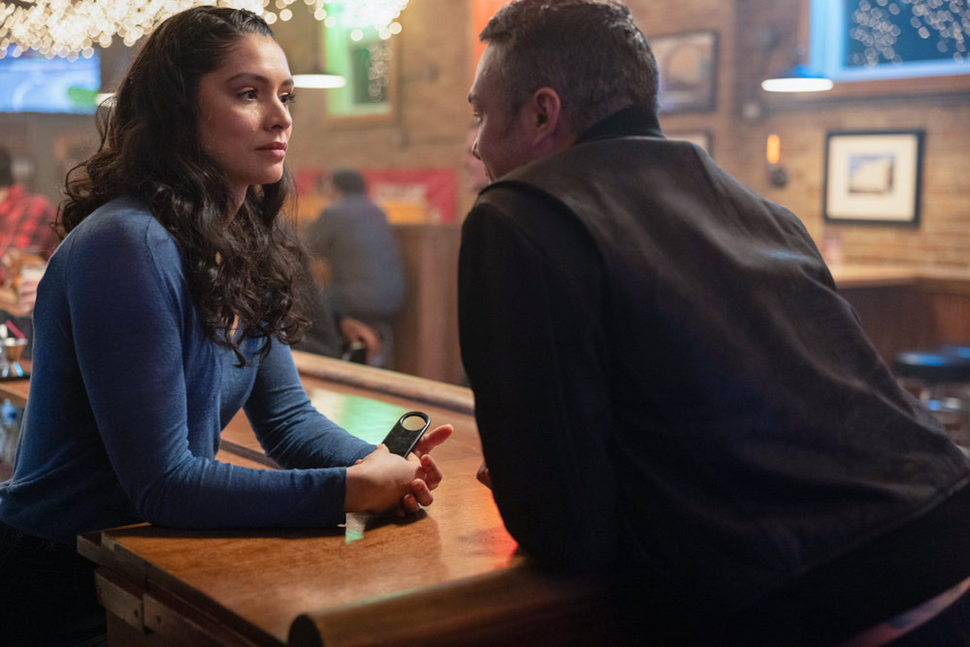 Miranda Rae Mayo as Stella Kidd and Taylor Kinney as Kelly Severide leaning over a table and talking intimately in 'Chicago Fire'