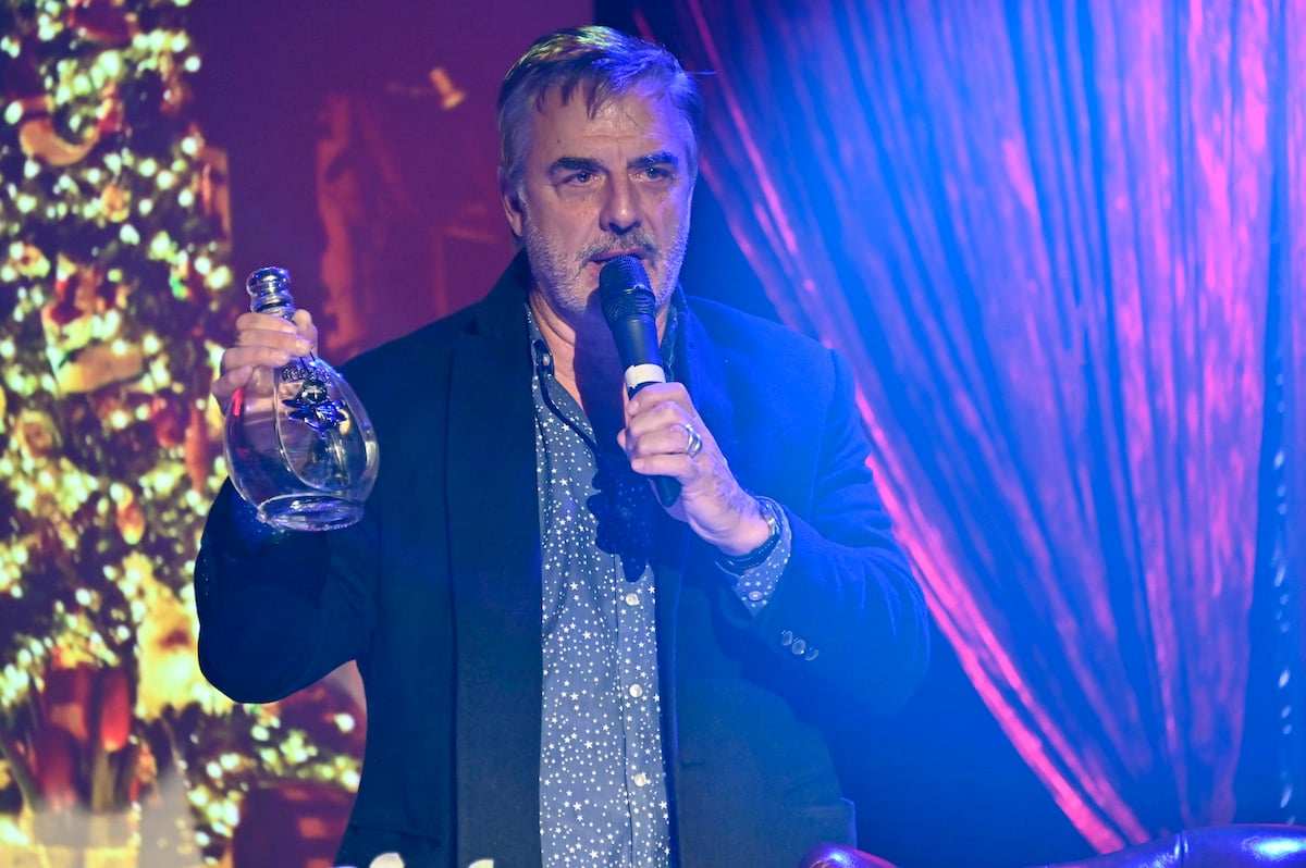 Chris Noth holds a microphone and a bottle of alcohol.