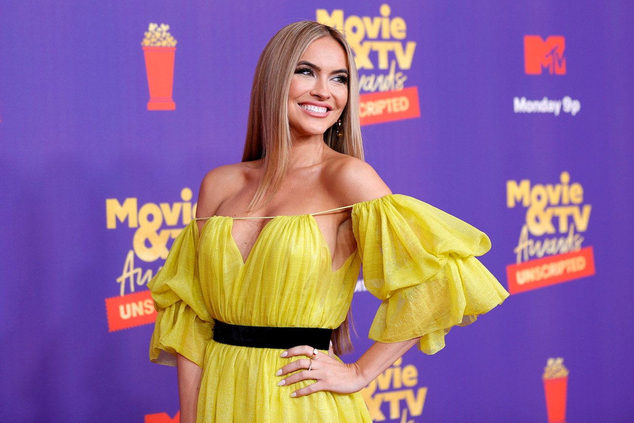 Chrishell Stause wearing a yellow dress in front of a purple background