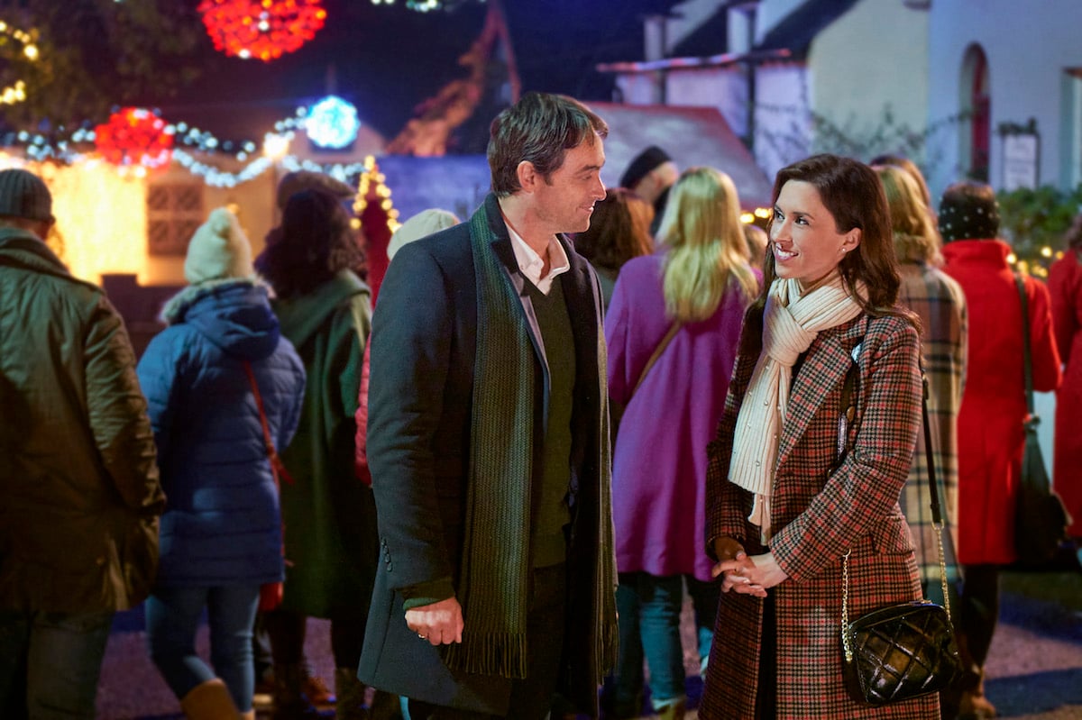 Stuart Townsend and Lacey Chabert, standing outside and wearing winter coats, in the Hallmark Channel movie 'Christmas at Castle Hart'