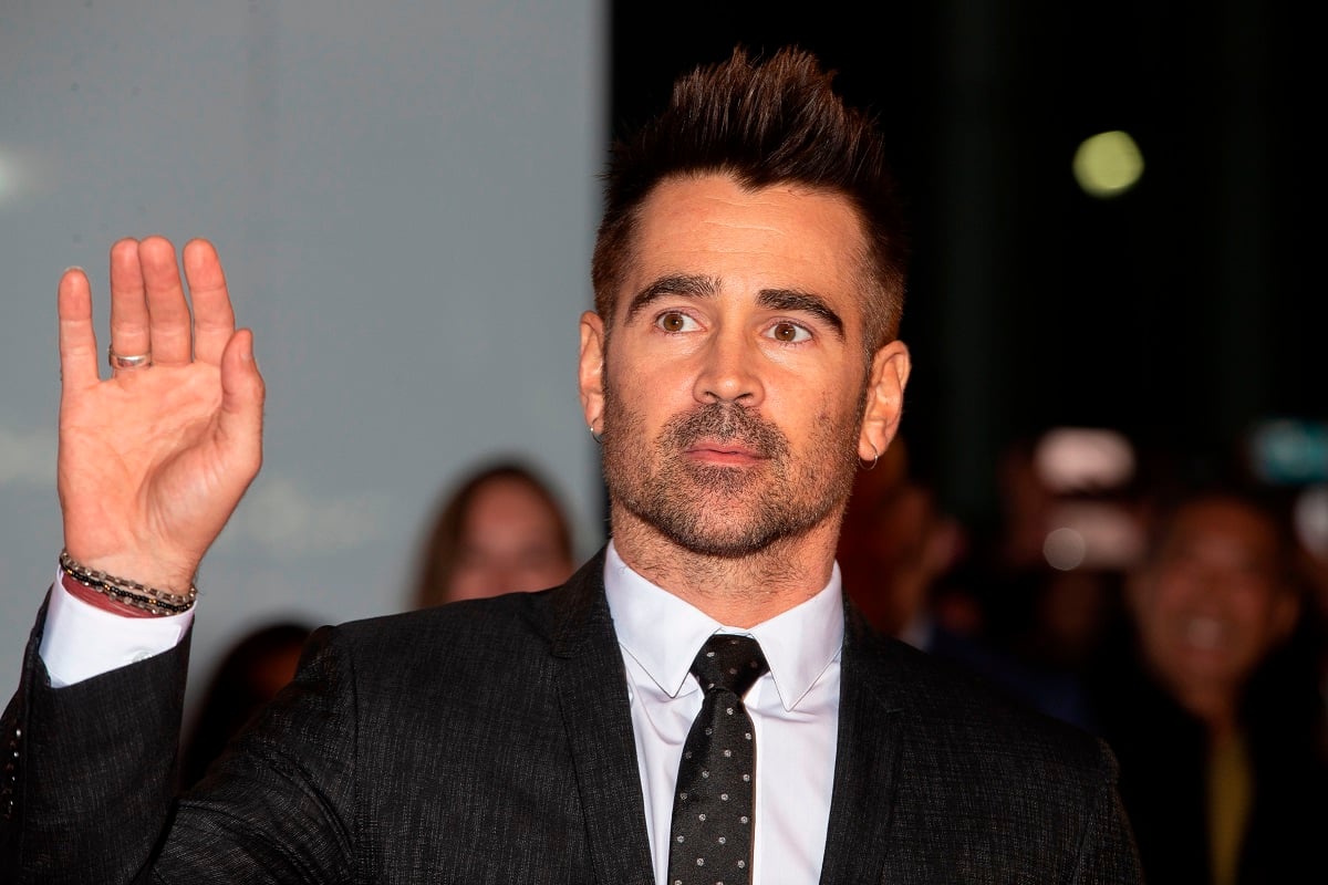 Colin Farrell posing in a business suit with his hand raised.