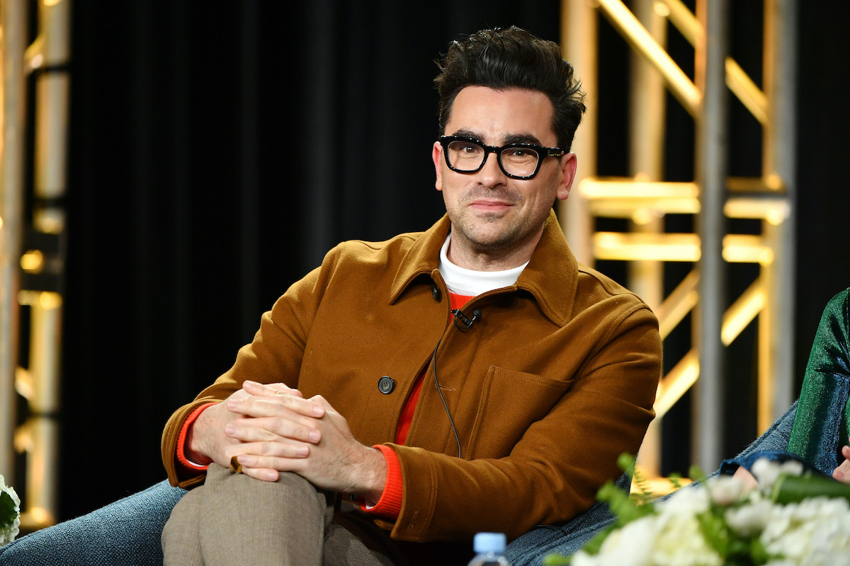 Schitt's Creek star Dan Levy smiles for the camera in a camel colored jacket